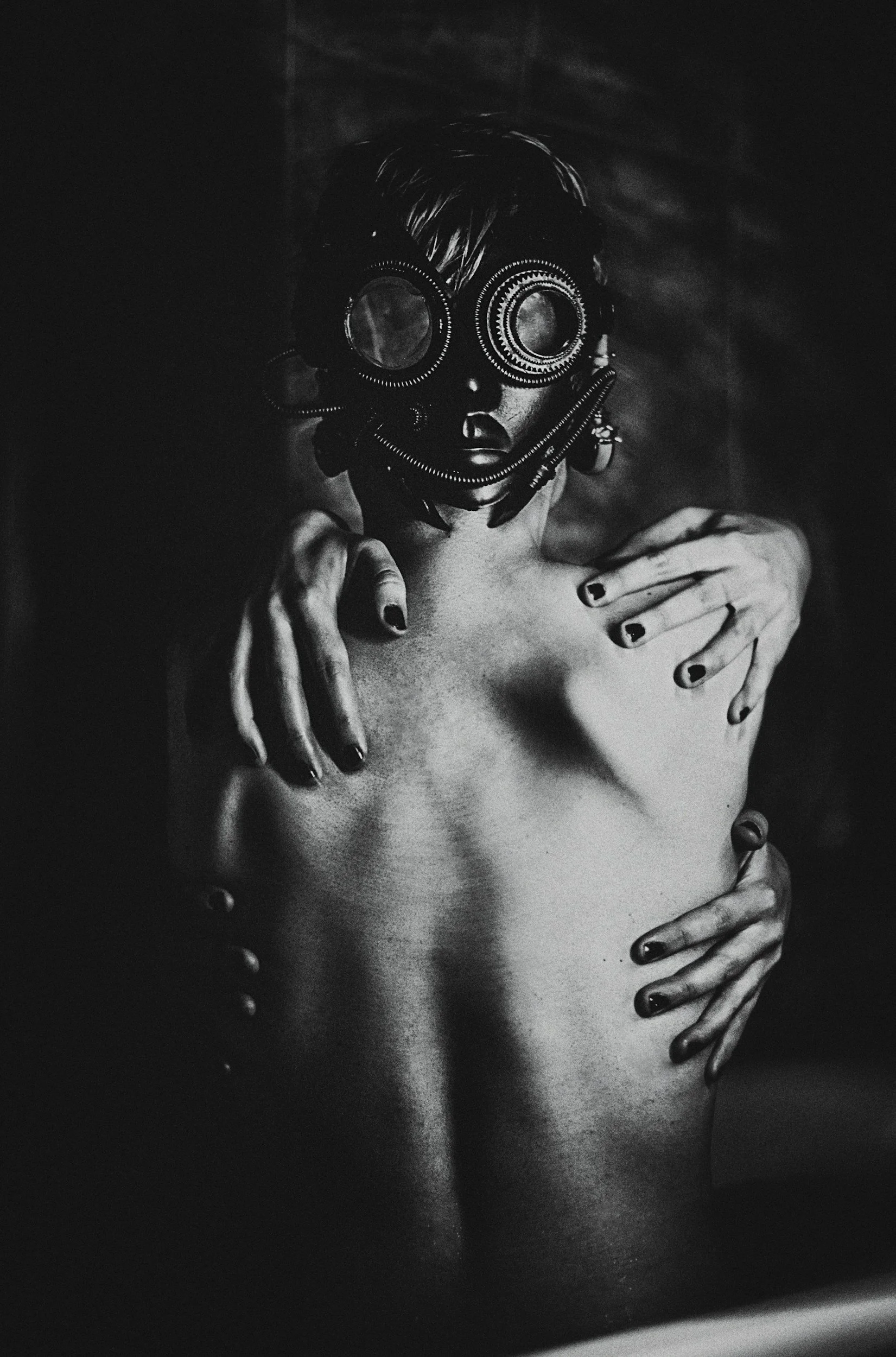 Black and white photo of a person wearing large goggles, with hands placed on their chest and waist, partially exposing their bare shoulder and chest.