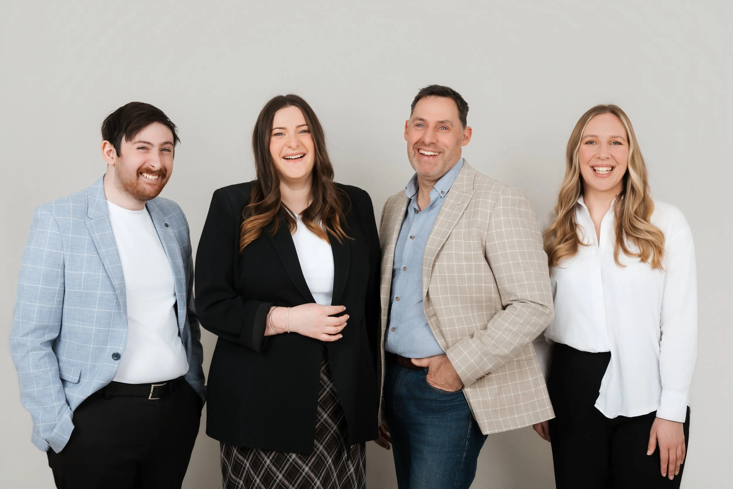 Group of four smiling business people standing against a plain gray wall.