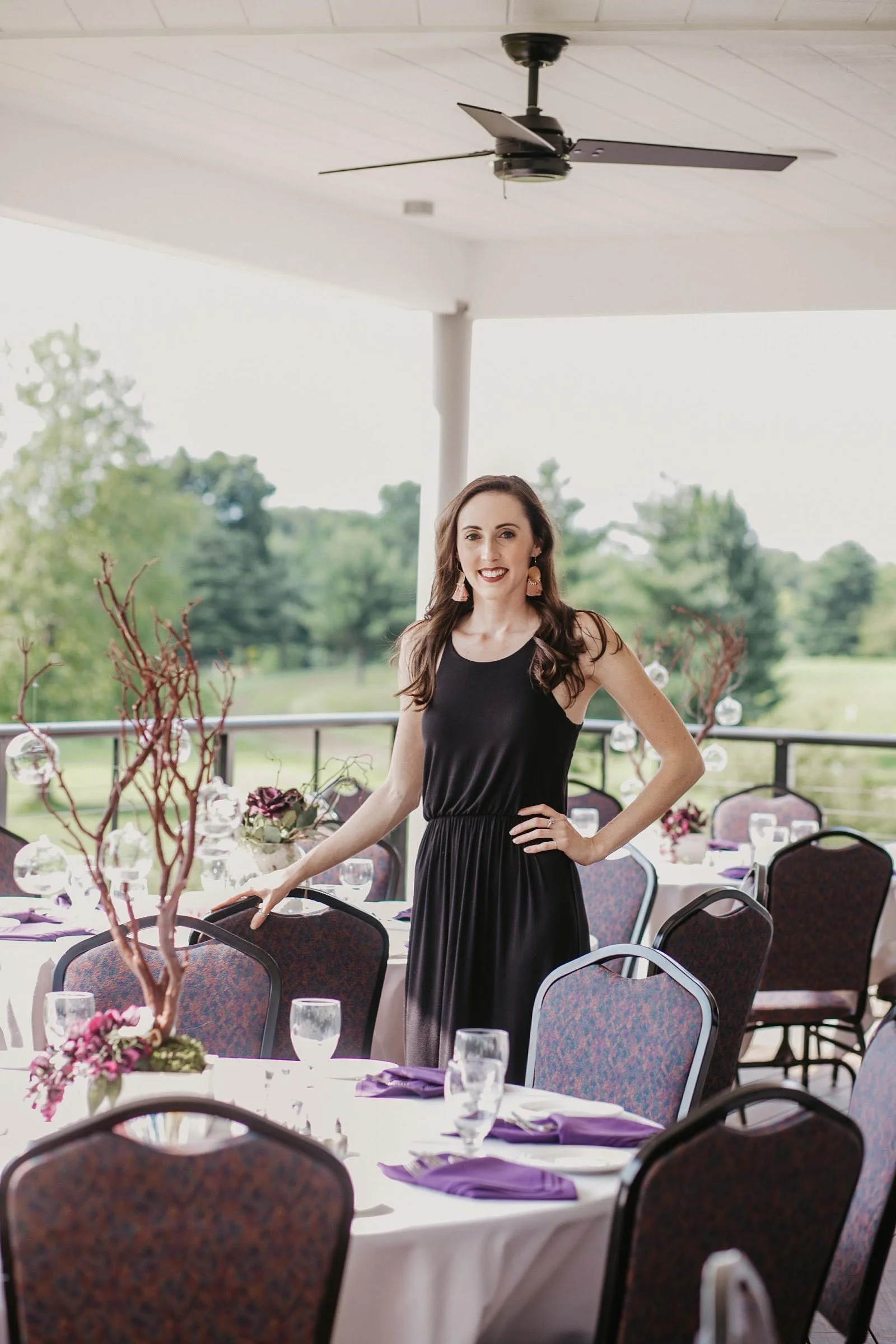 Planned Chaos wedding planning consultant standing among set reception tables with manzanita centerpieces and purple napkins