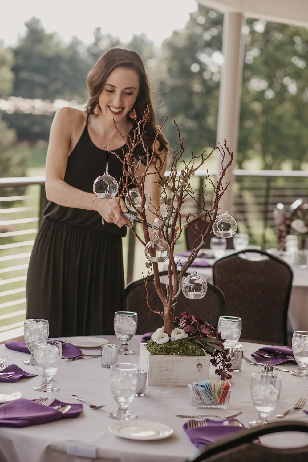Lighting tea lights in glass globes hanging from a manzanita branch centerpiece at a wedding reception table