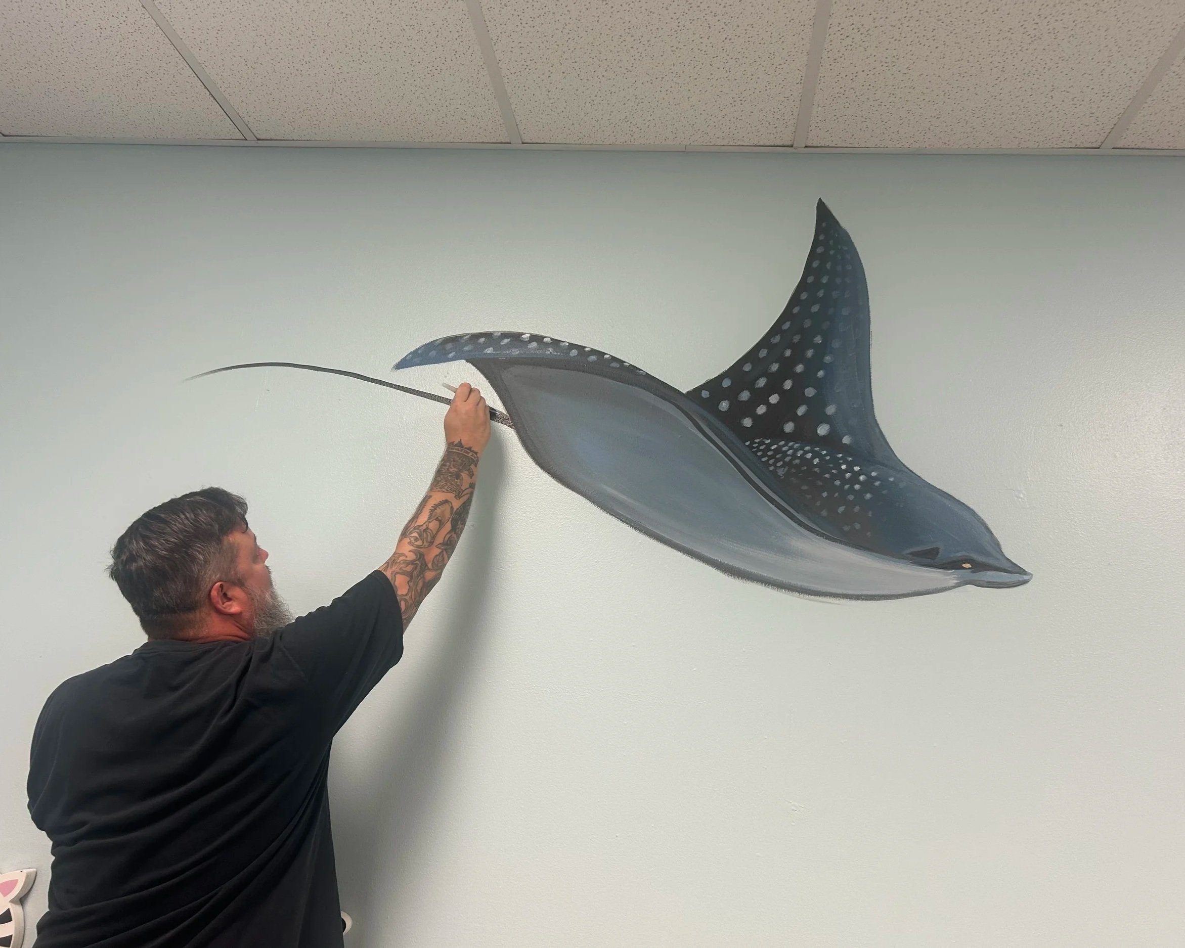 A man is painting a sting ray on a wall