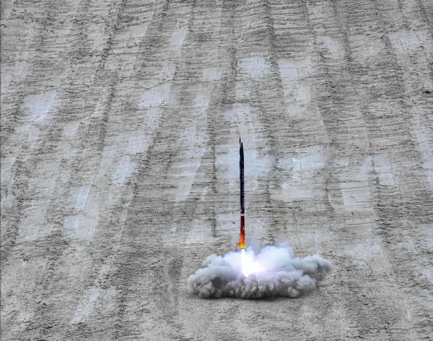 Rocket launching with exhaust and smoke against a dirt ground.