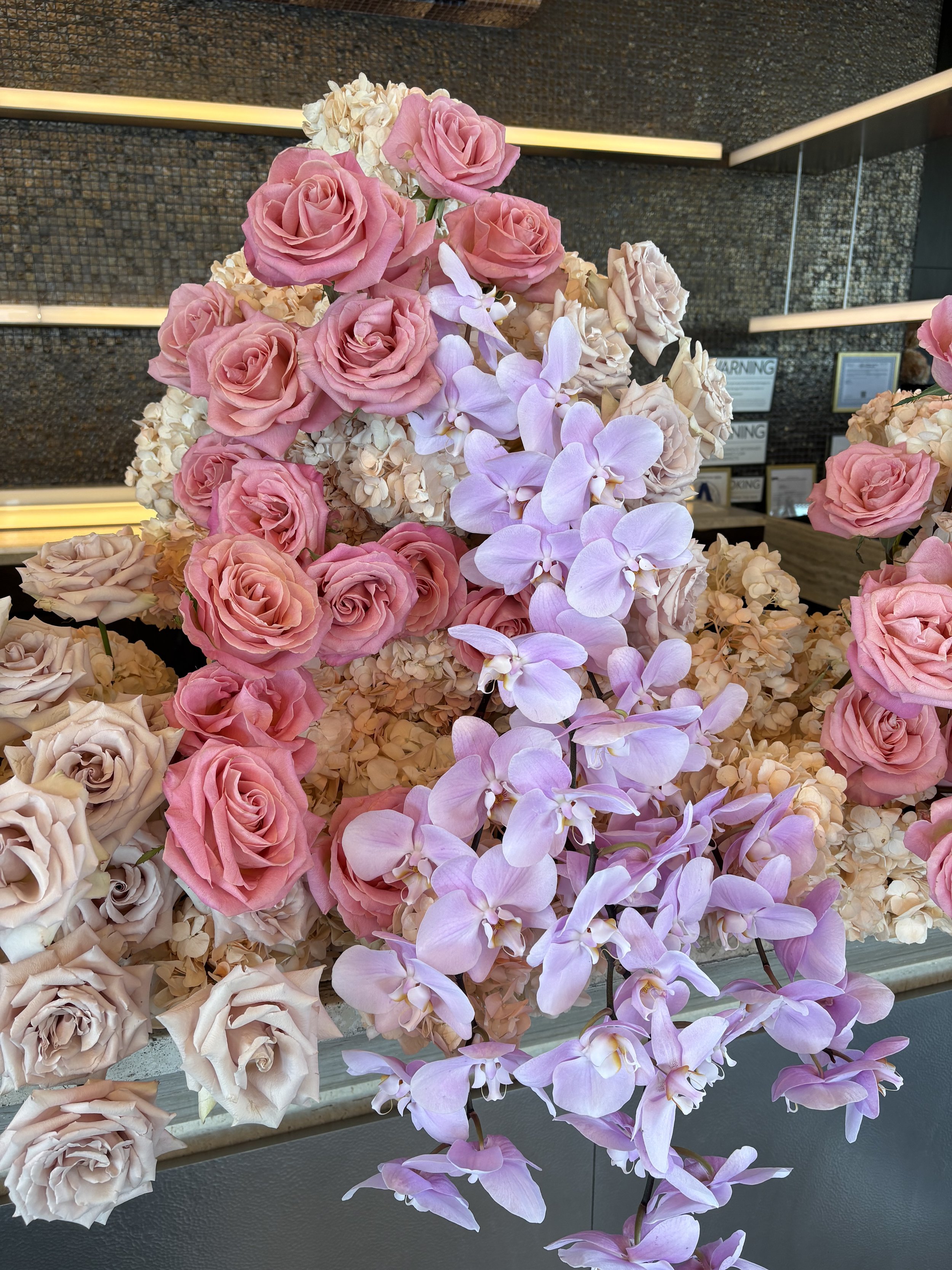 A floral arrangement featuring pink roses, white hydrangeas, and light purple orchids.