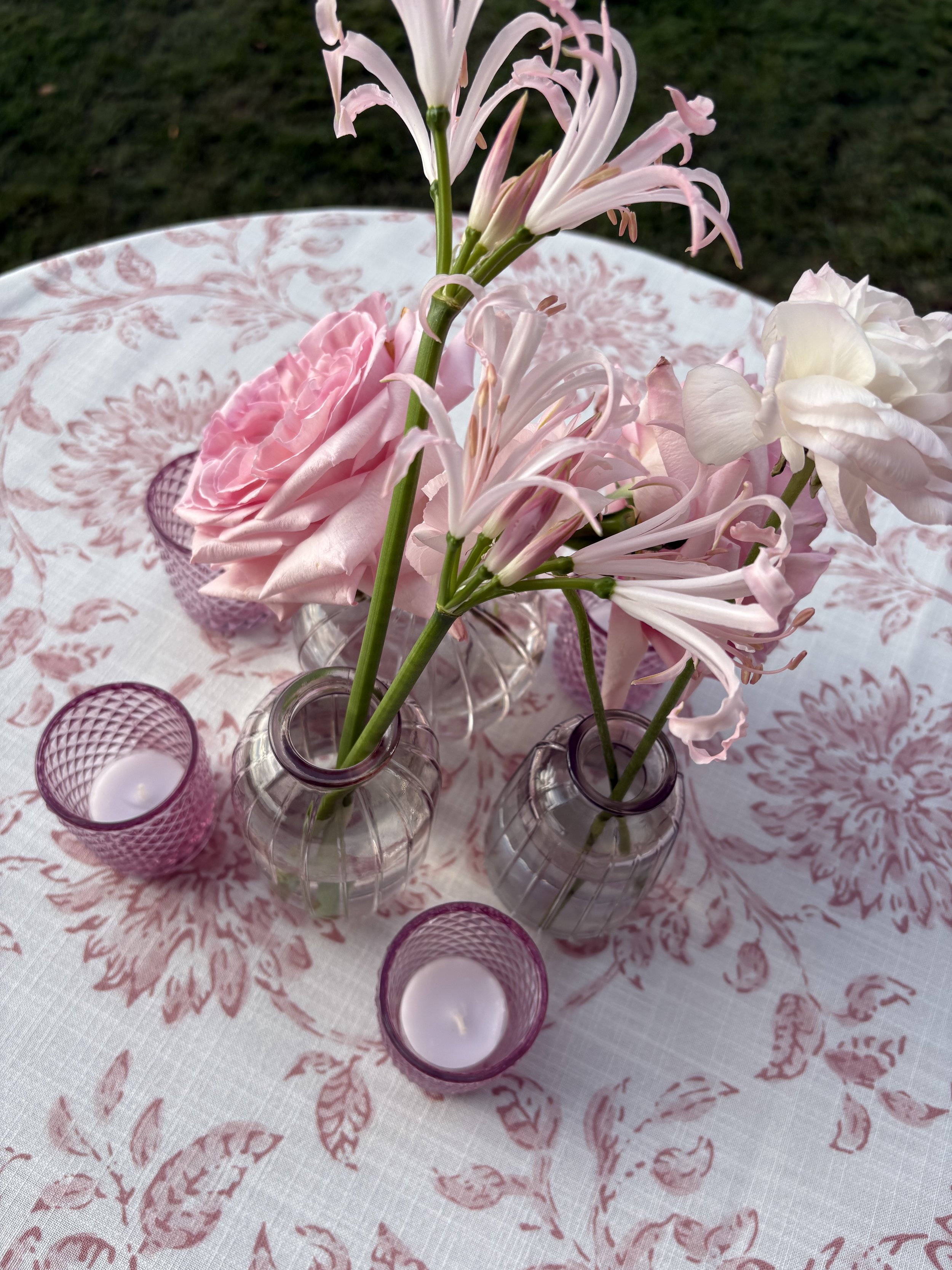 Close-up of pink and white flowers in small glass vases on a pink and white patterned tablecloth.