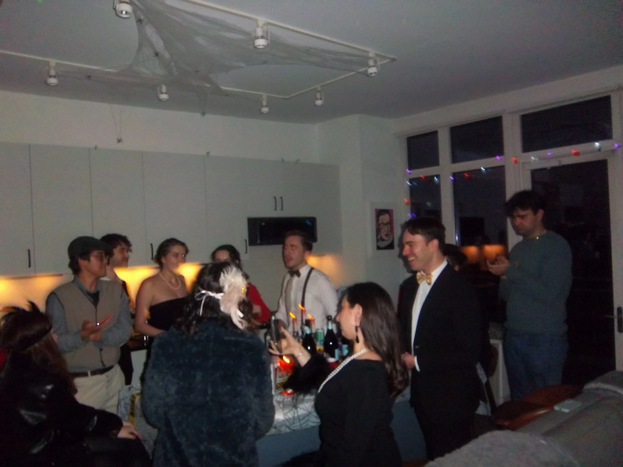 People gather around a table with wine bottles in a room decorated for a celebration, possibly a birthday or special event.