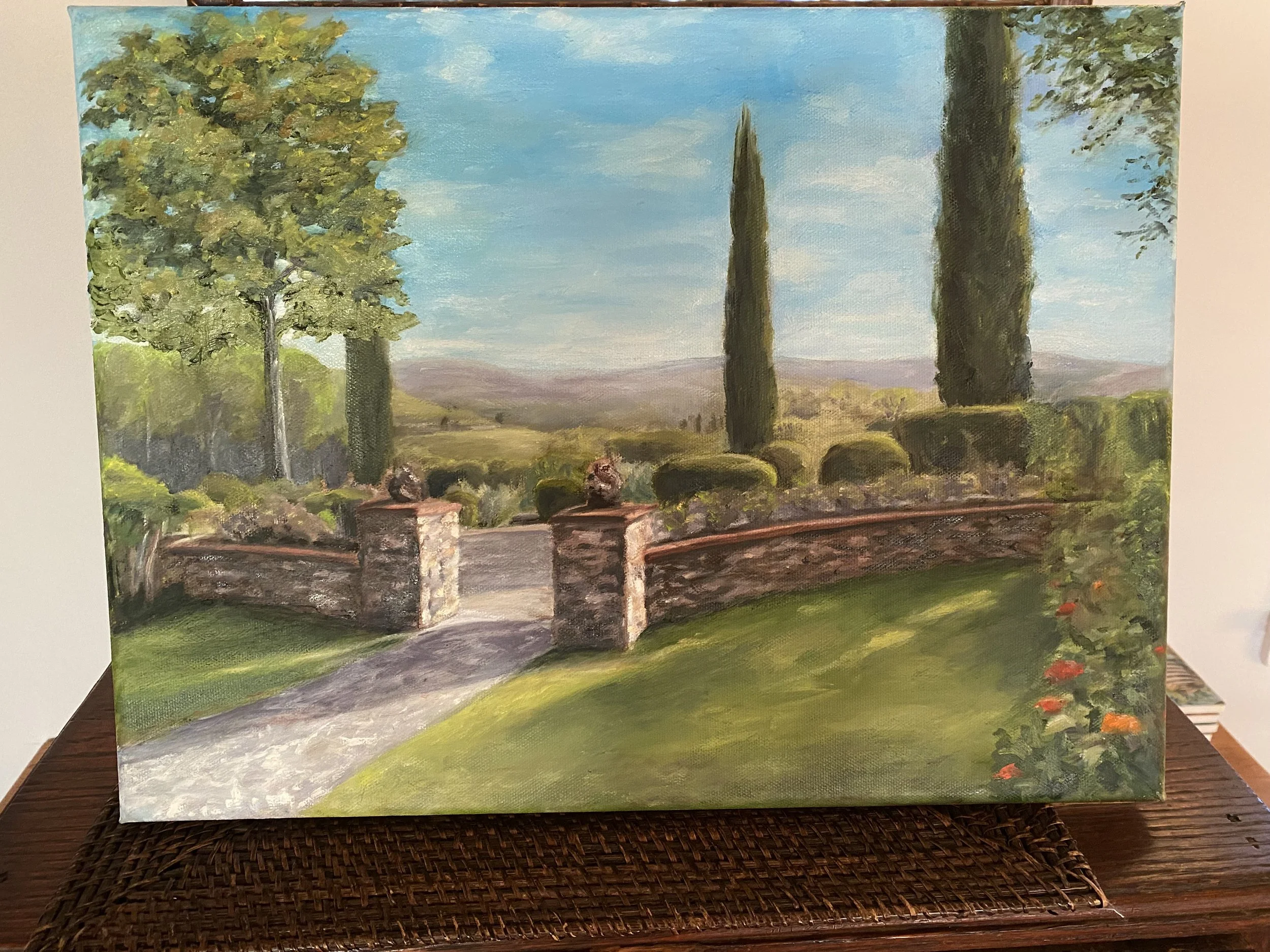 Landscape painting featuring a view of a blue sky with some clouds, tall cypress trees, and rolling hills in the background. There is a stone wall with a gate in the foreground and lush greenery surrounding it.
