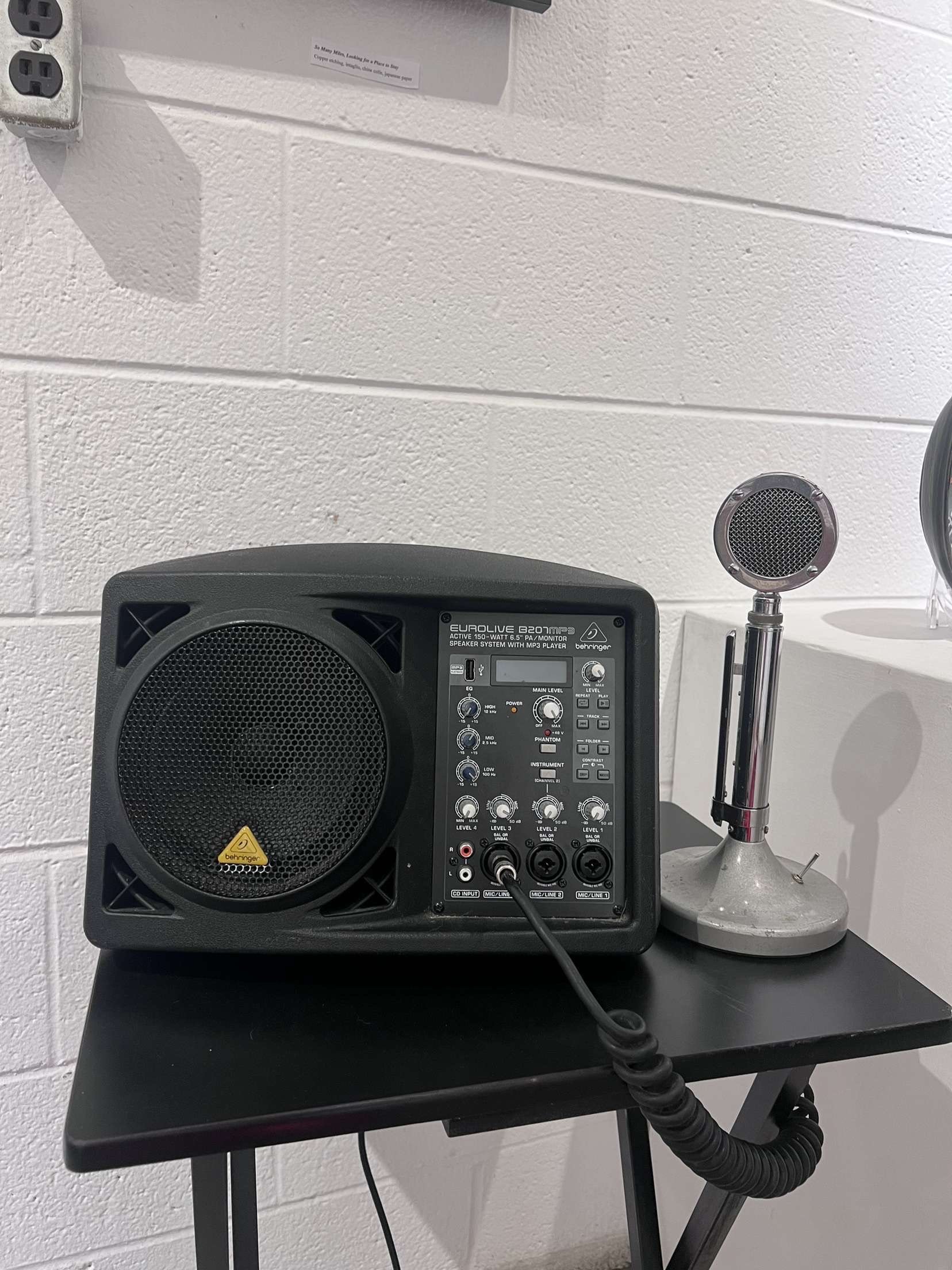 A small speaker and microphone on a black table against a white brick wall.