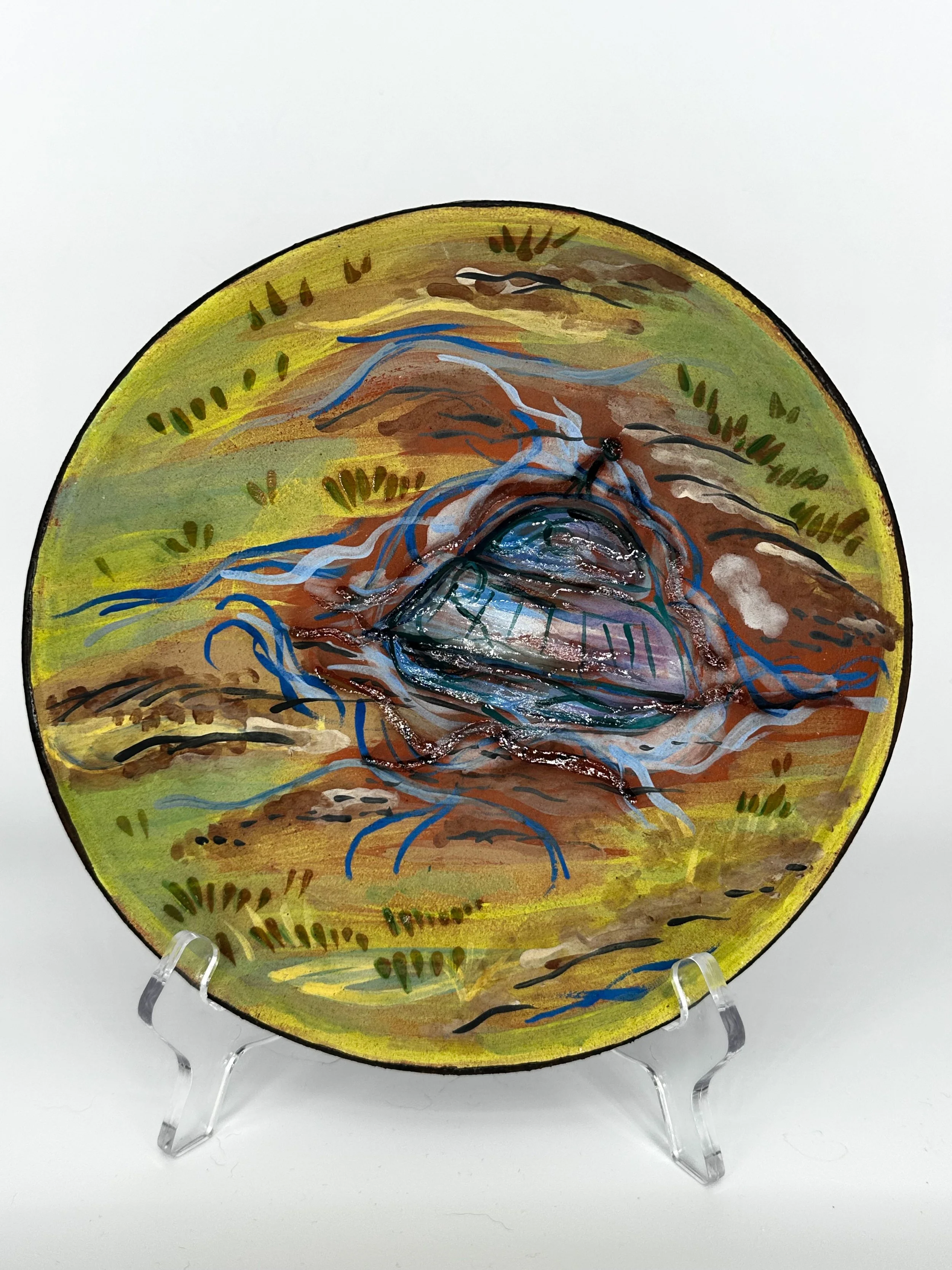 Painted decorative ceramic plate featuring an image of a hologram of a UFO crashed onto a patch of grass and dirt. 