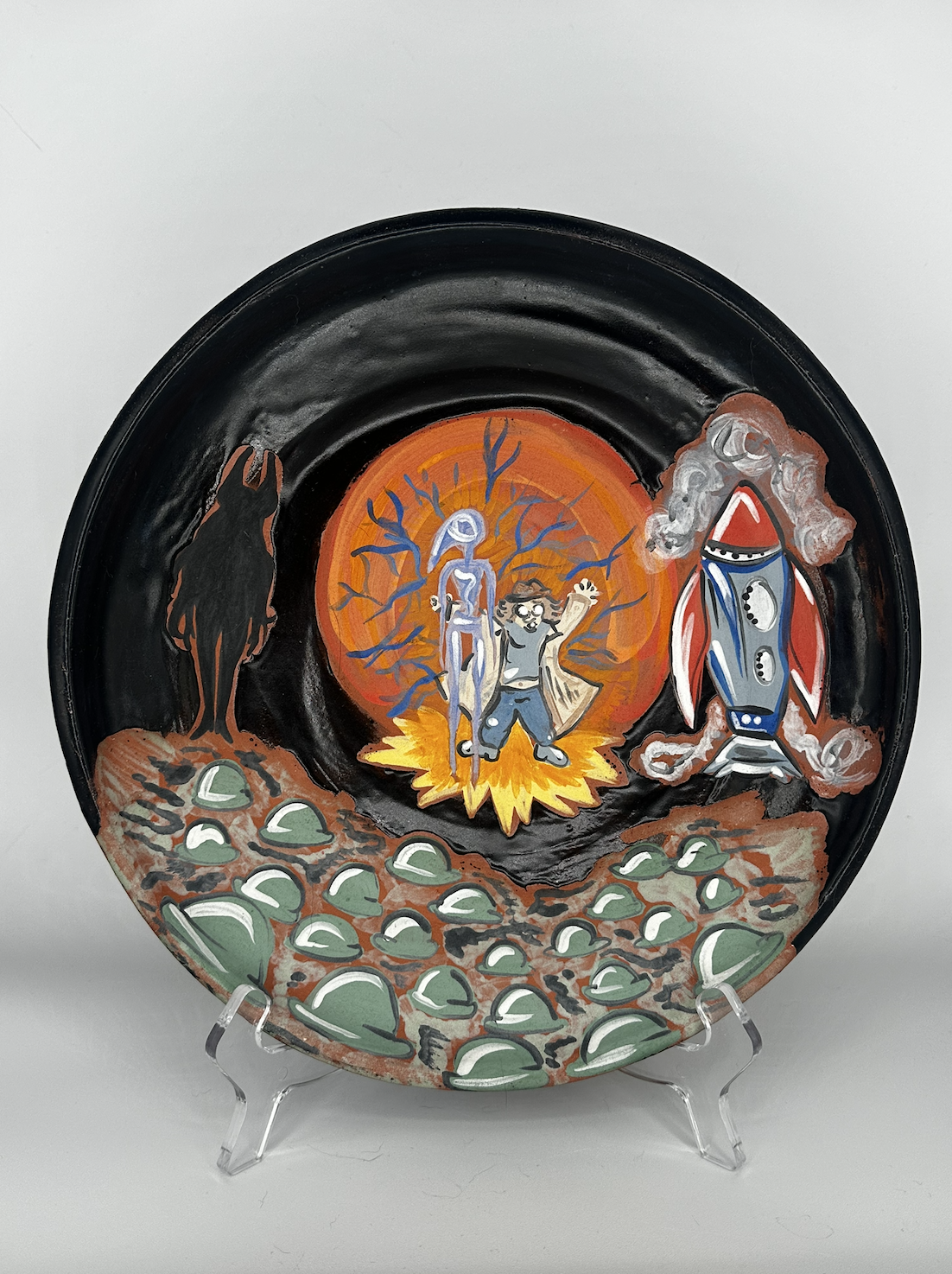 Decorative painted plate featuring a black background, a central explosion with a human figure and a robotic figure, surrounded by a tree, a rocket, a dog, and green rocks.