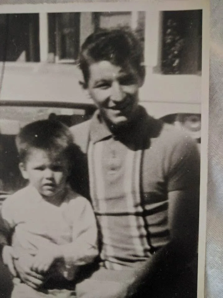 A black and white photo shows a smiling woman holding a young girl in front of a house or building with windows.