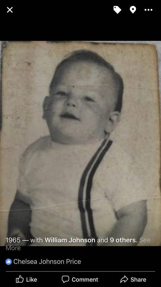 Black and white photo of a young boy with short hair, wearing a t-shirt with dark stripes on the sleeves.