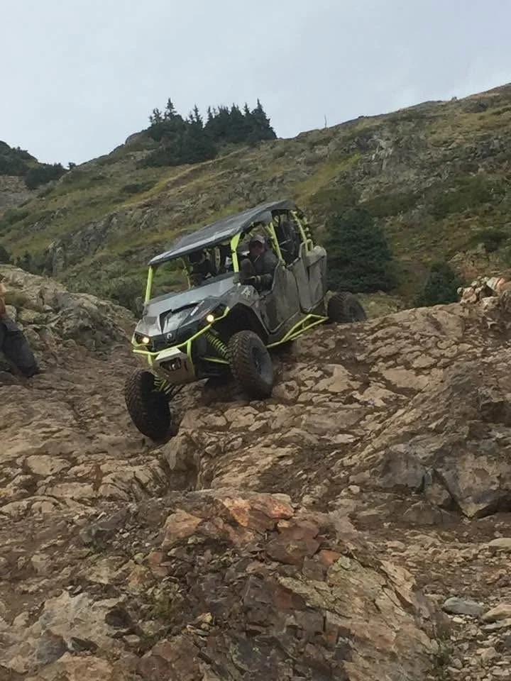 An off-road utility vehicle navigating a rocky hillside in a mountainous landscape.