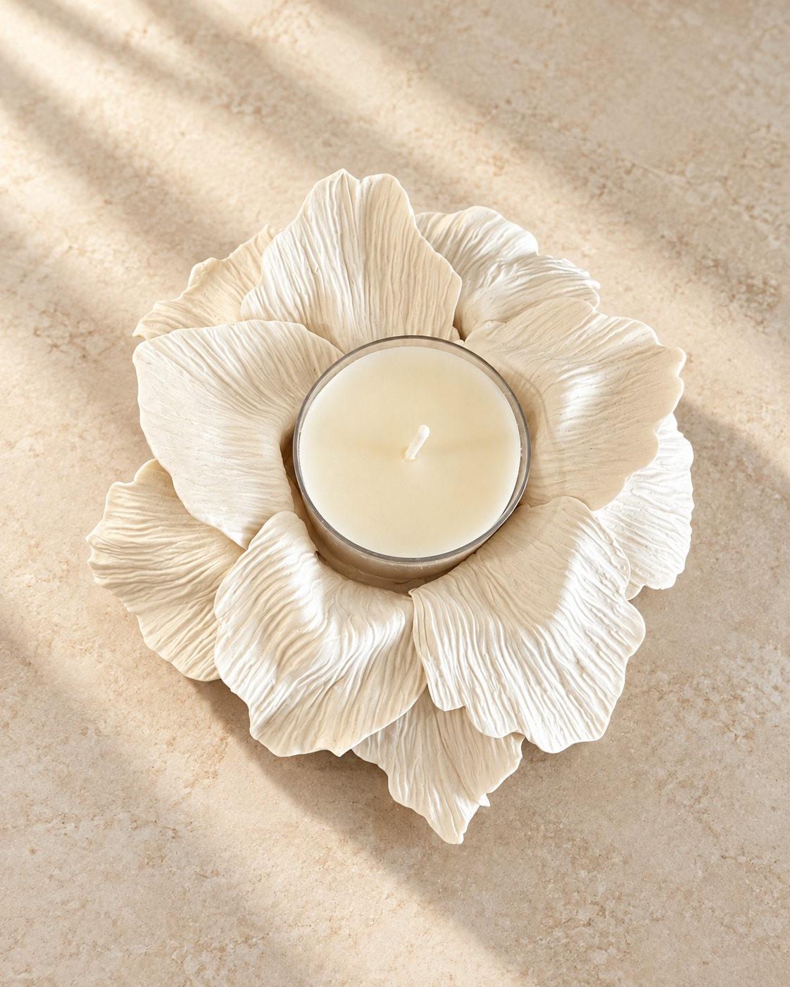 An overhead view of an intricately sculpted, off-white polymer clay candle holder shaped like a blooming flower with textured petals, holding a glass-cased wax votive candle on a neutral background.