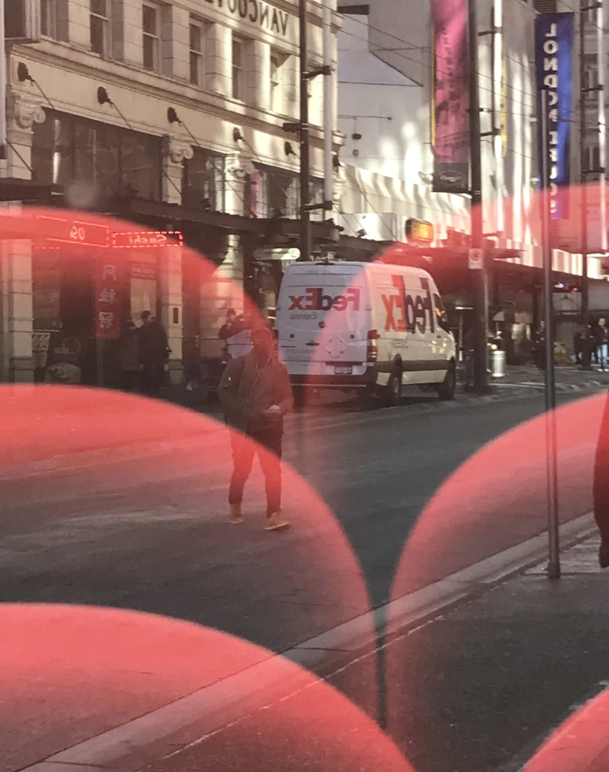 Urban street scene featuring a pedestrian, buildings and a vehicle, layered with a dramatic red lens flare and double-exposure effect.