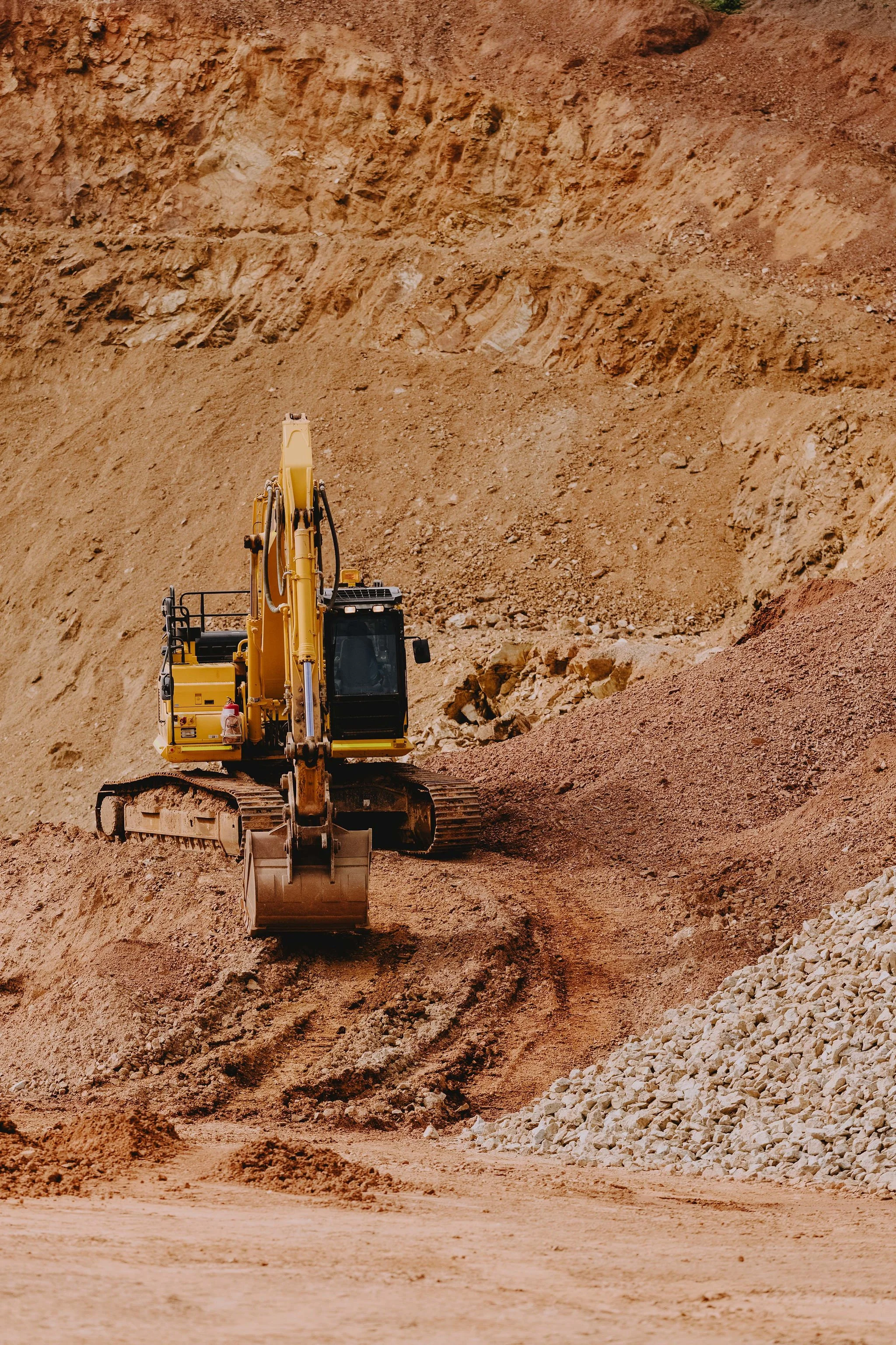 A yellow excavator operating at a construction site with dirt and rocks piled around.