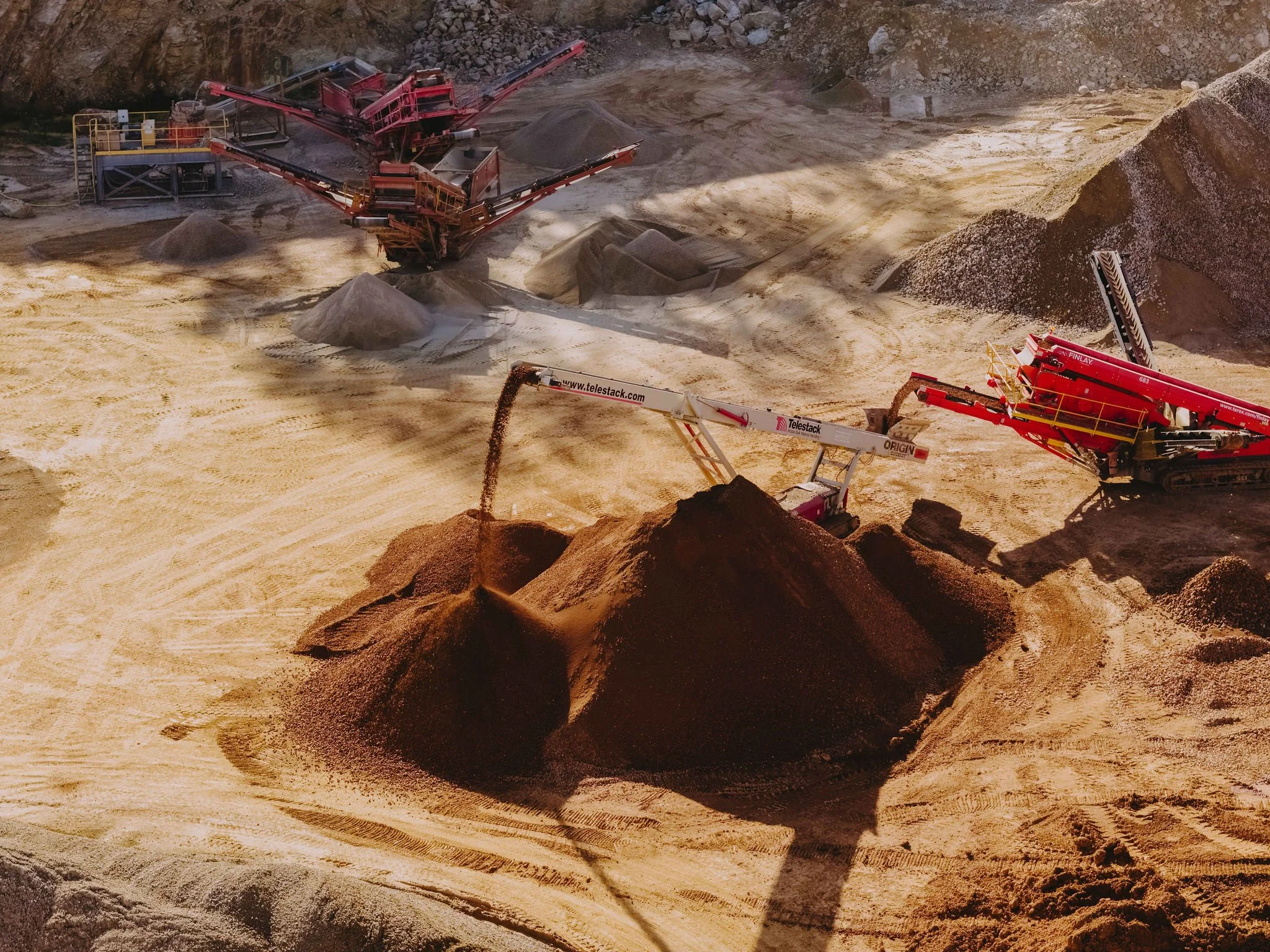 View of a quarry with large piles of gravel and sand, industrial machinery, and conveyor belts.