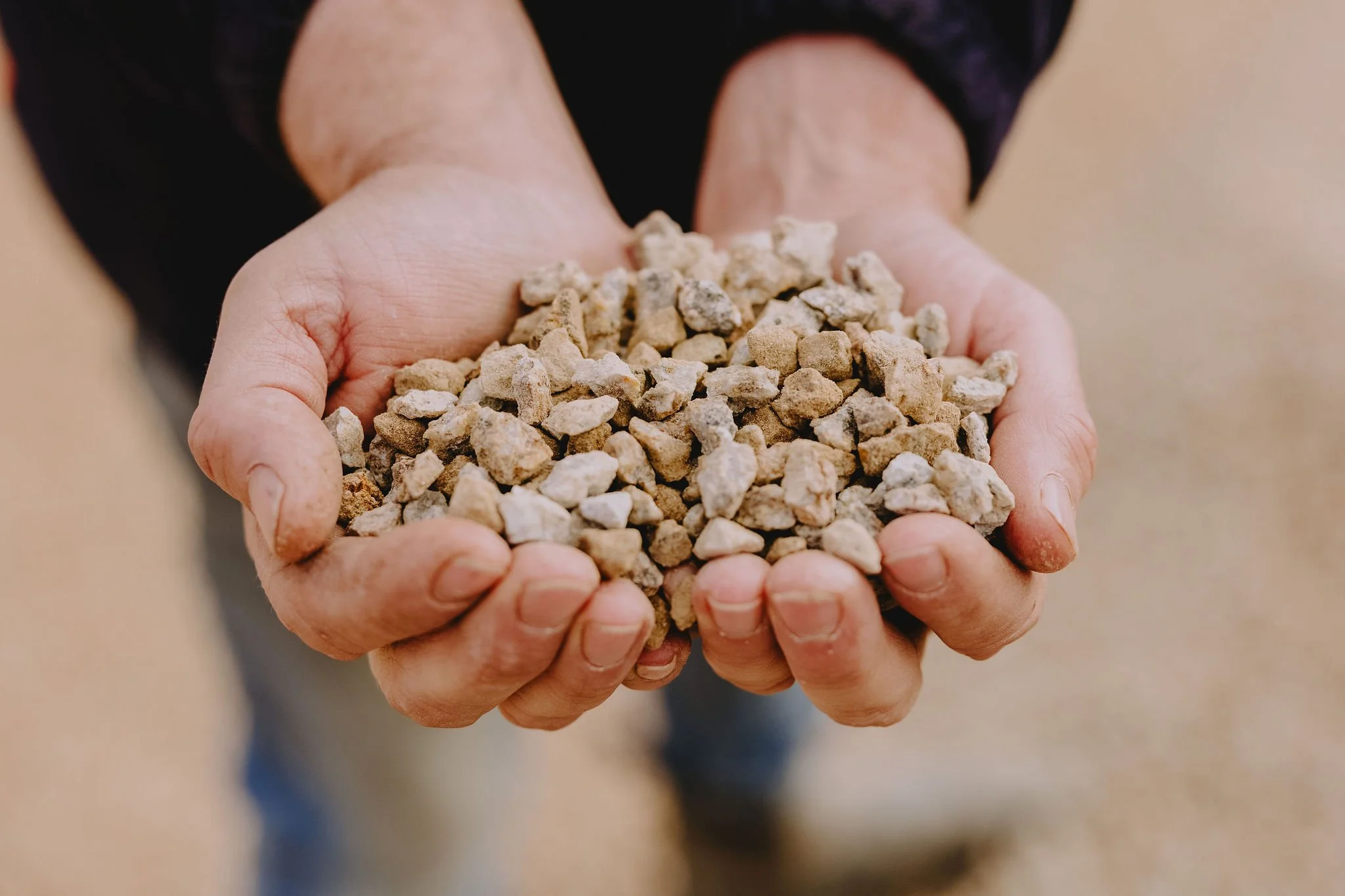 Hands holding a handful of small rocks or gravel.