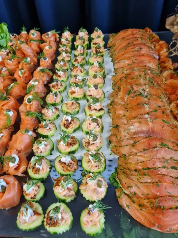 Tray of gourmet hors d'oeuvres including smoked salmon bites, cucumber rounds topped with salmon and garnishes, and smoked salmon slices with herbs.