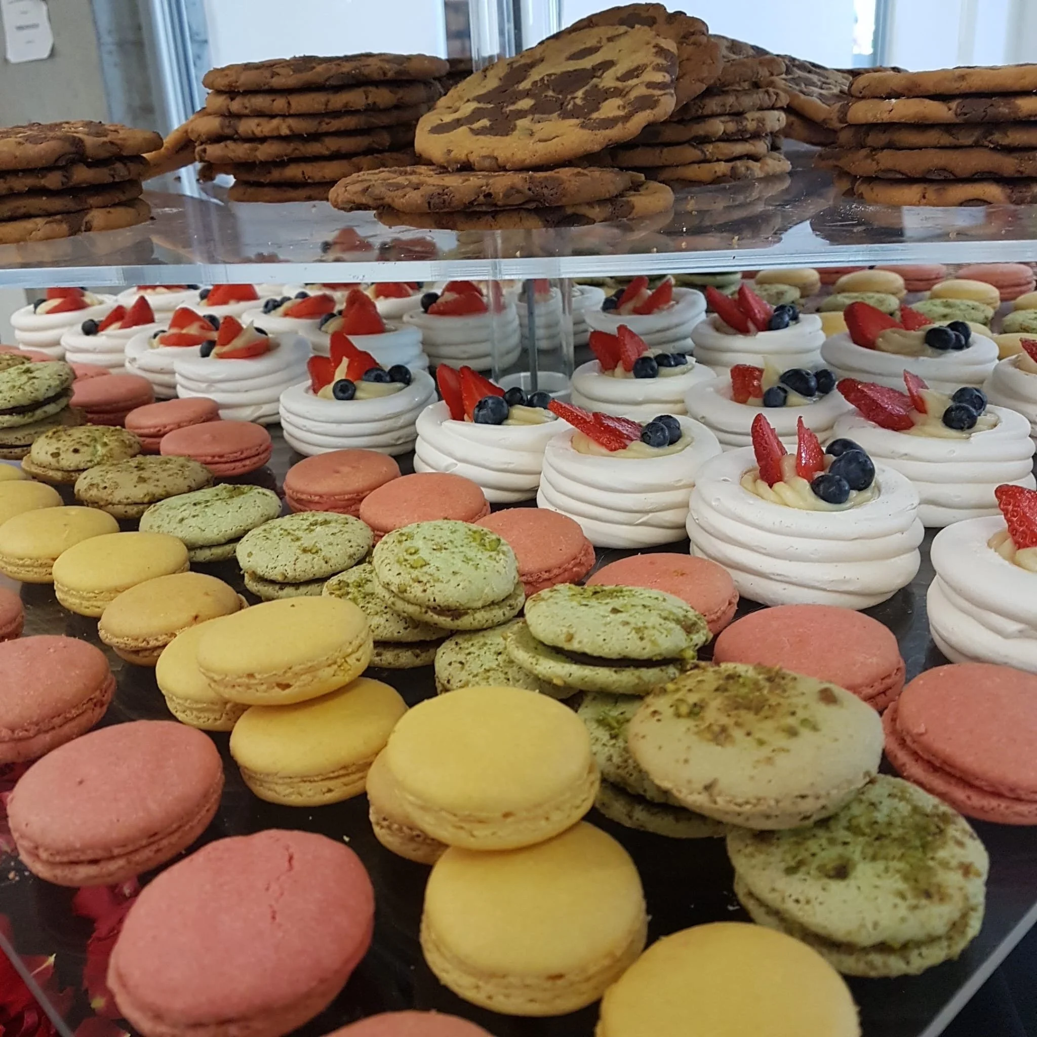 A display of assorted cookies and macarons arranged on a multi-tiered stand, including chocolate chip cookies and fruit-topped meringue cookies.