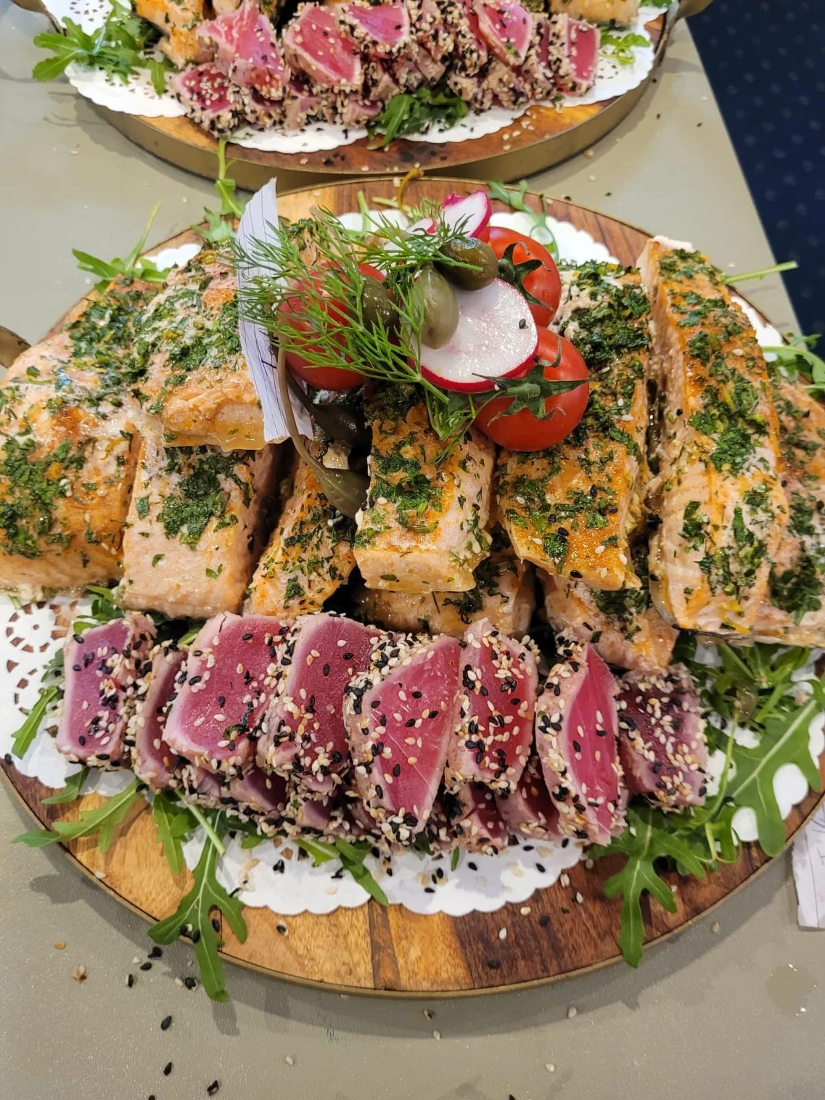 Assorted raw fish and seafood sashimi platter with herbs, greens, and vegetables garnishes, served on wooden platters decorated with sesame and herbs.