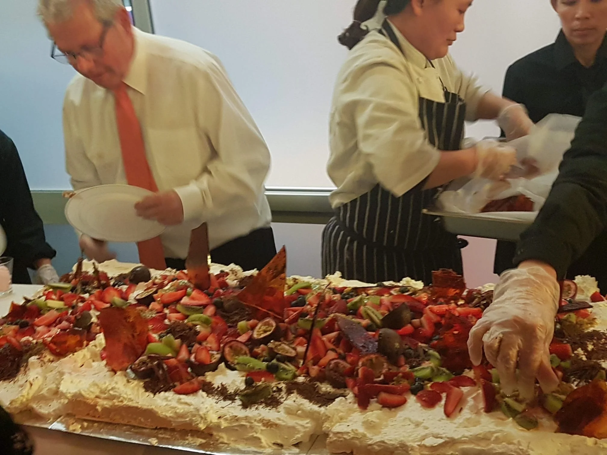 People serving themselves from a large table of assorted cakes and desserts at a buffet or celebration event.