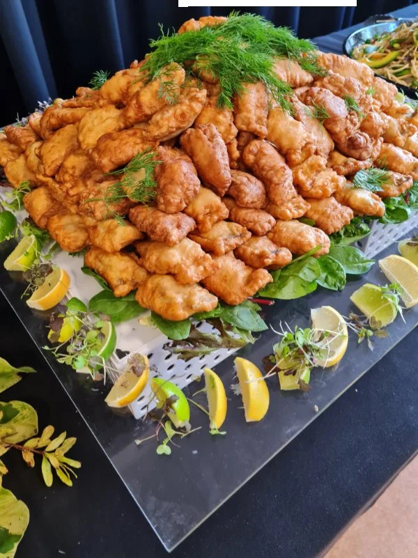 A large pile of fried chicken pieces garnished with fresh herbs and lemon wedges, arranged on a platter with decorative greens around the edge.