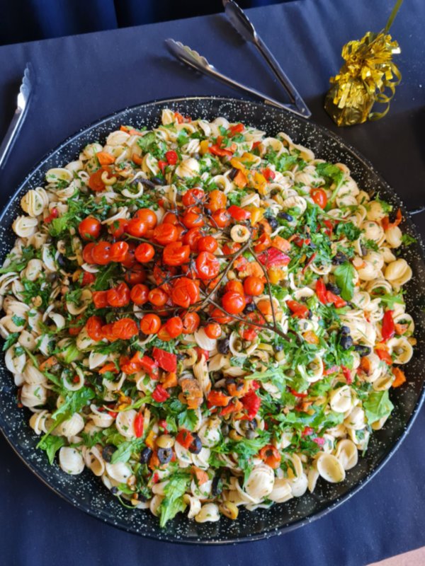 Large serving dish of pasta salad with cherry tomatoes, mixed greens, and chopped vegetables.