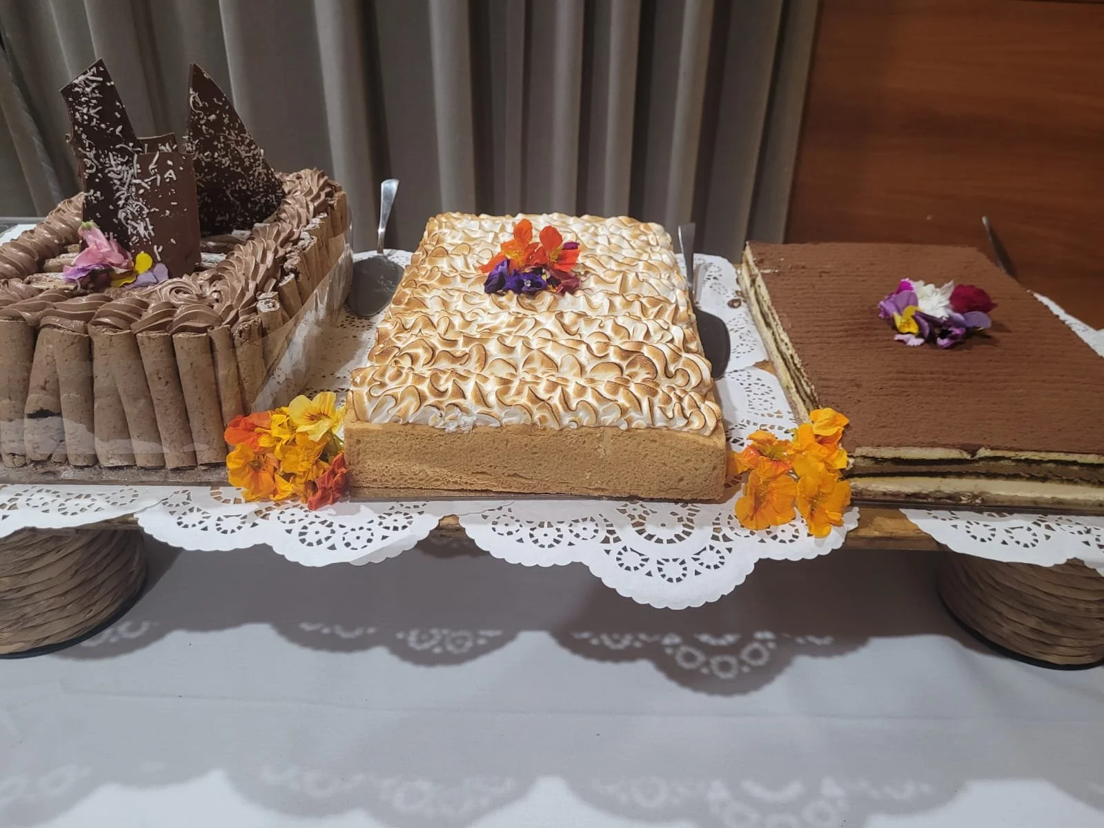 Assorted cakes on a lace-covered table, decorated with colorful edible flowers.