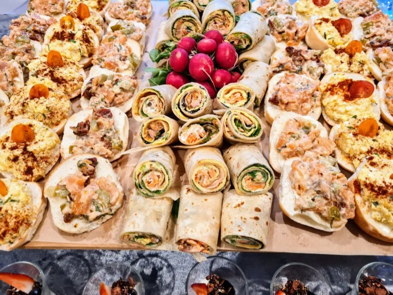 Assorted appetizer platter with bread and vegetable bites, roll-ups with vegetables and meat, and a bunch of red radishes in the center.