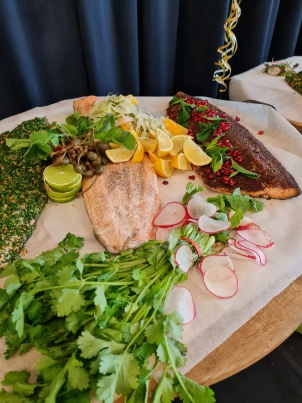 Assorted cooked and raw seafood with herbs, radishes, lemon wedges, and greens on a wooden board.