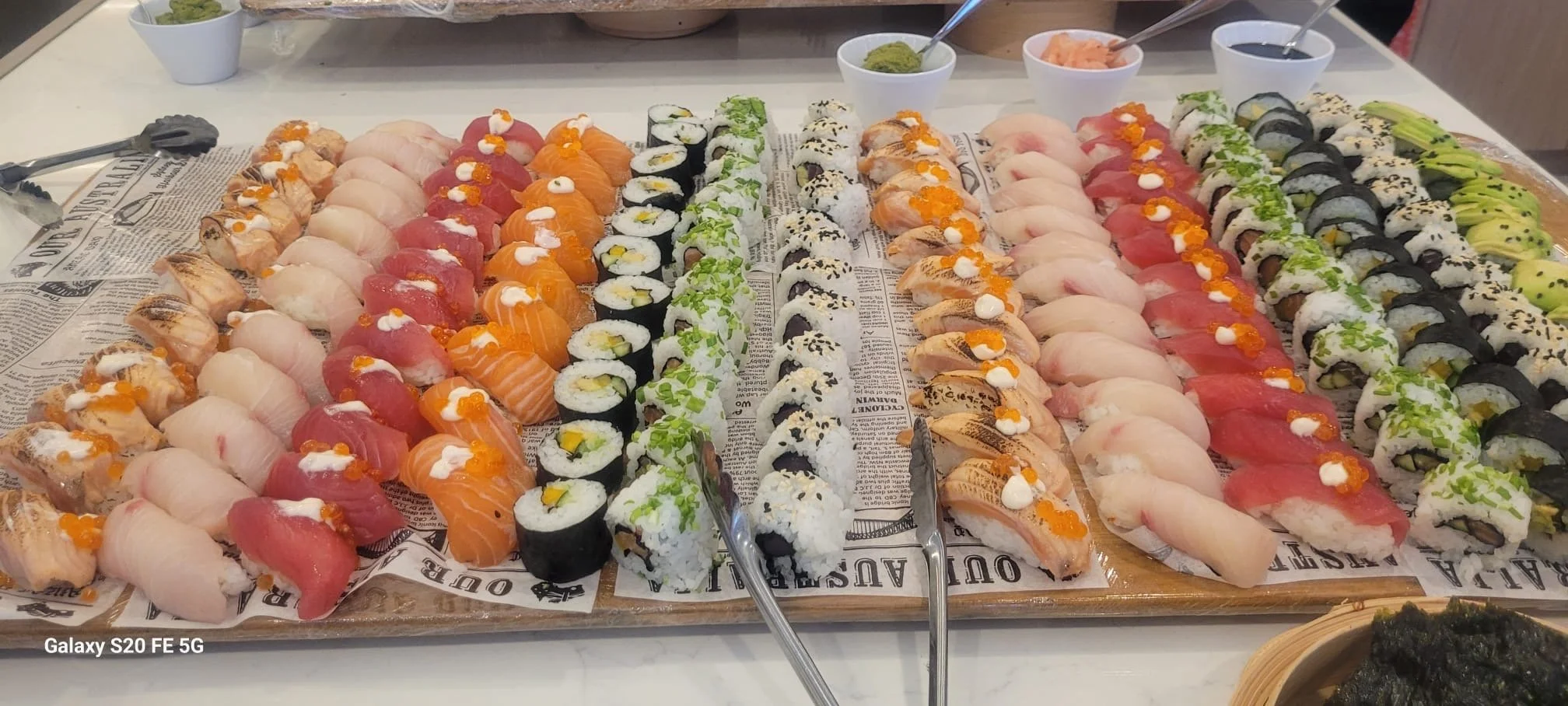 Assorted sushi rolls and sashimi arranged on a tray covered with printed paper.