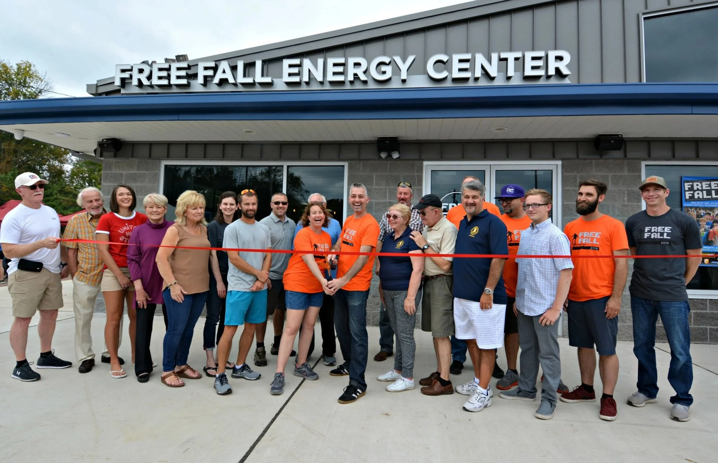 Group of people standing in front of a building with a sign that says 'Free Fall Energy Center'; during a ribbon-cutting ceremony.