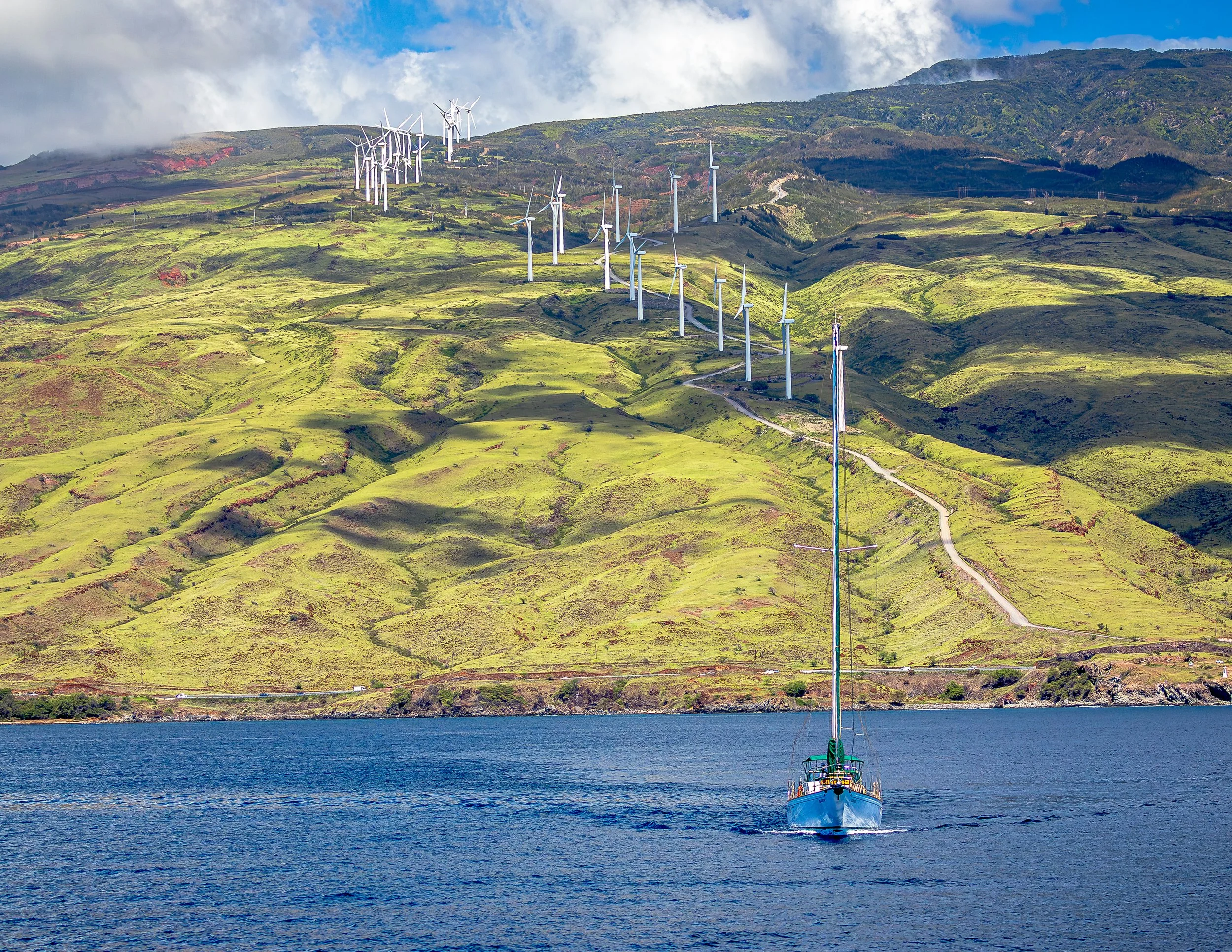 A boat sailing on a body of water with green hills and wind turbines in the background.