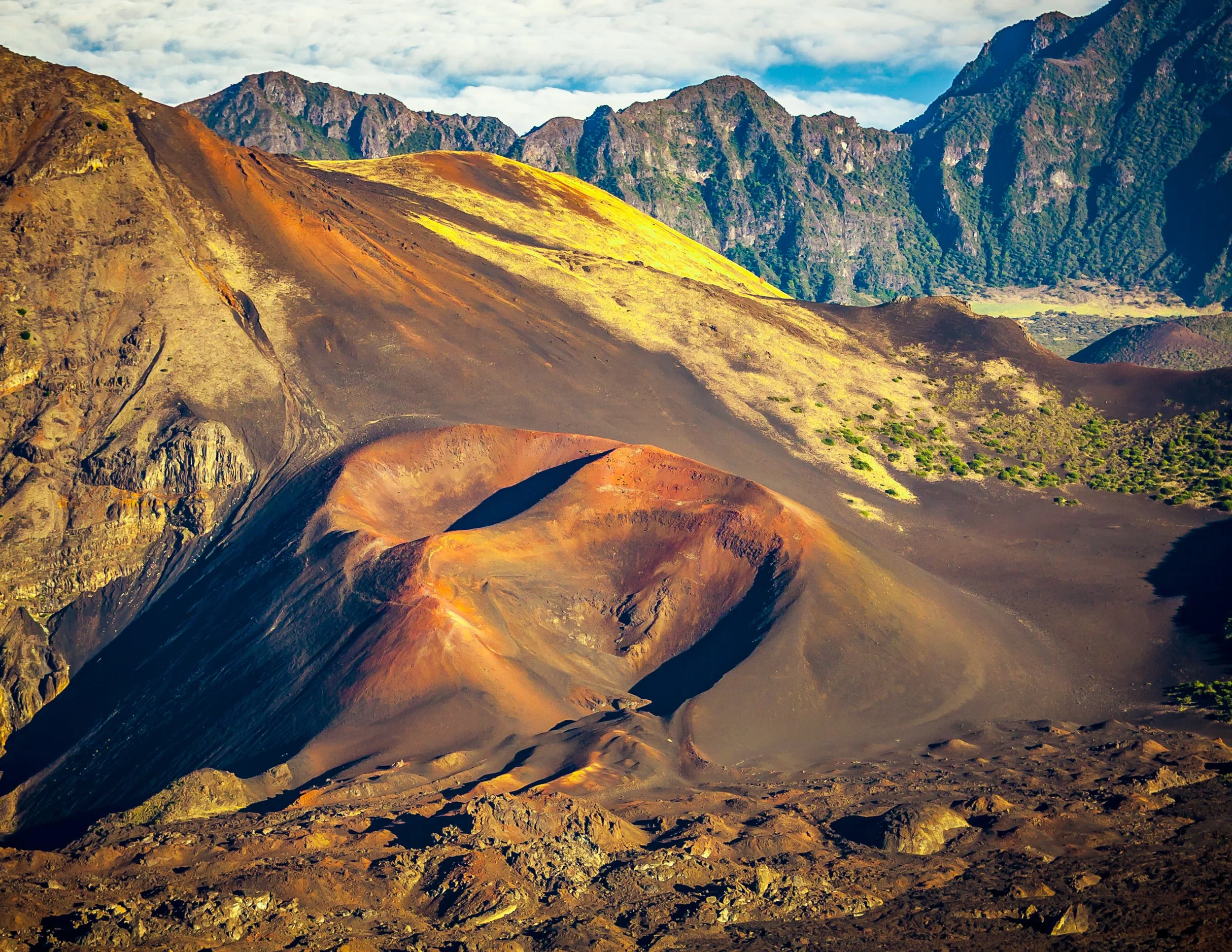 Colorful volcanic mountain landscape with steep slopes and rugged terrain, under a partly cloudy sky.