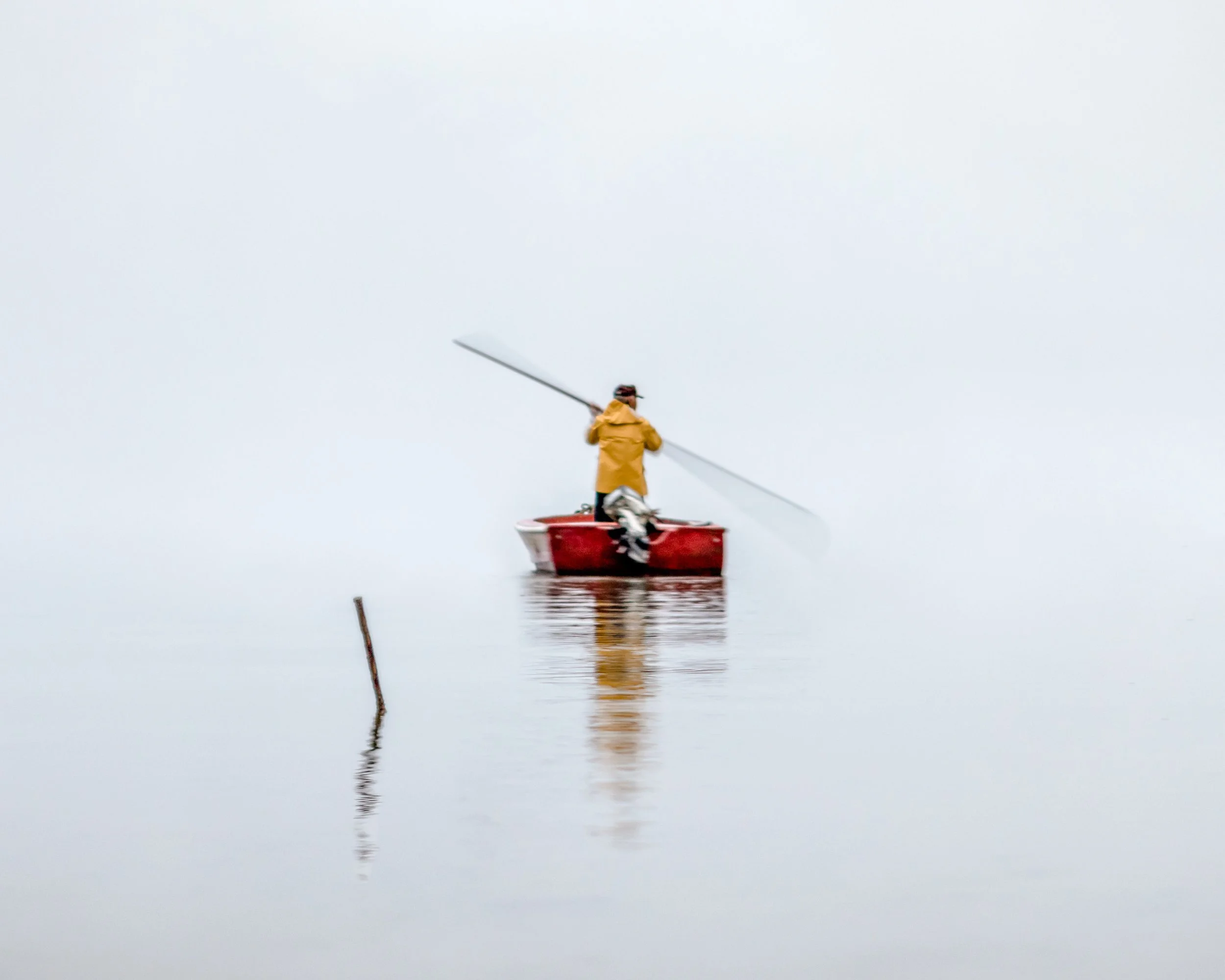 Person in yellow jacket ice skating on a frozen lake during overcast weather, with their reflection visible in the ice.