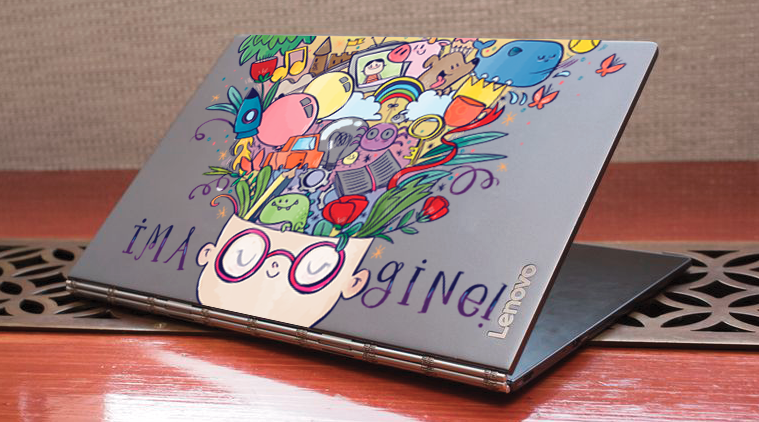 Closed silver Lenovo laptop with colorful doodle art on the lid, featuring a person with glasses and various vibrant cartoon-like images emerging from their head, placed on a wooden surface.