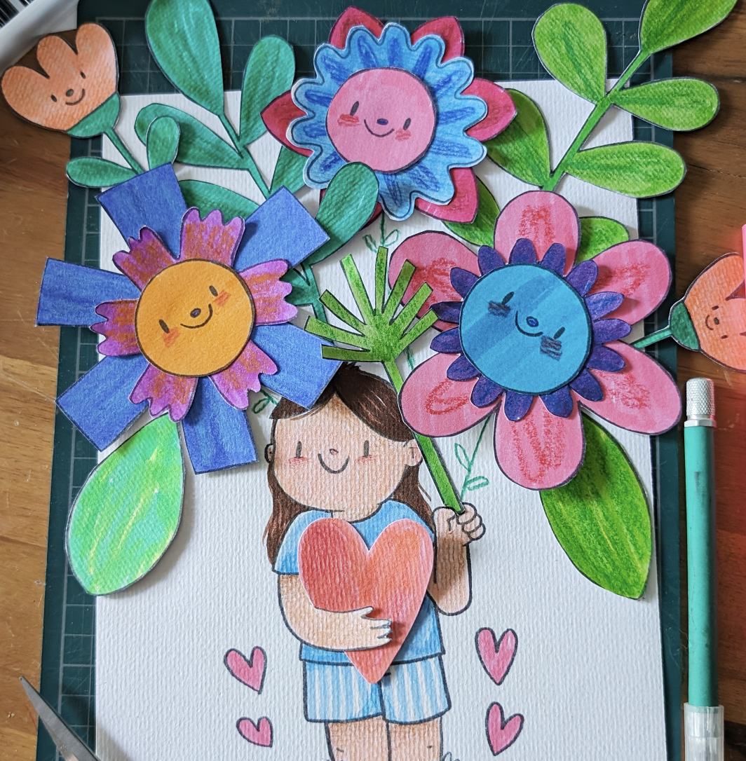 Colorful hand-drawn paper craft depicting a girl holding a heart-shaped object surrounded by large, smiling cartoon flowers with faces, green leaves, and small pink hearts.