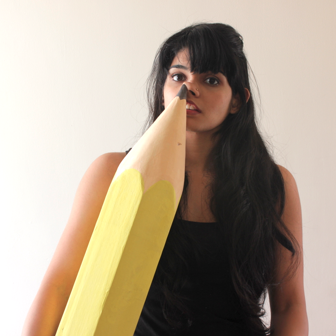 Young woman with long dark hair, black tank top, holding a large yellow pencil, standing against a plain white wall.
