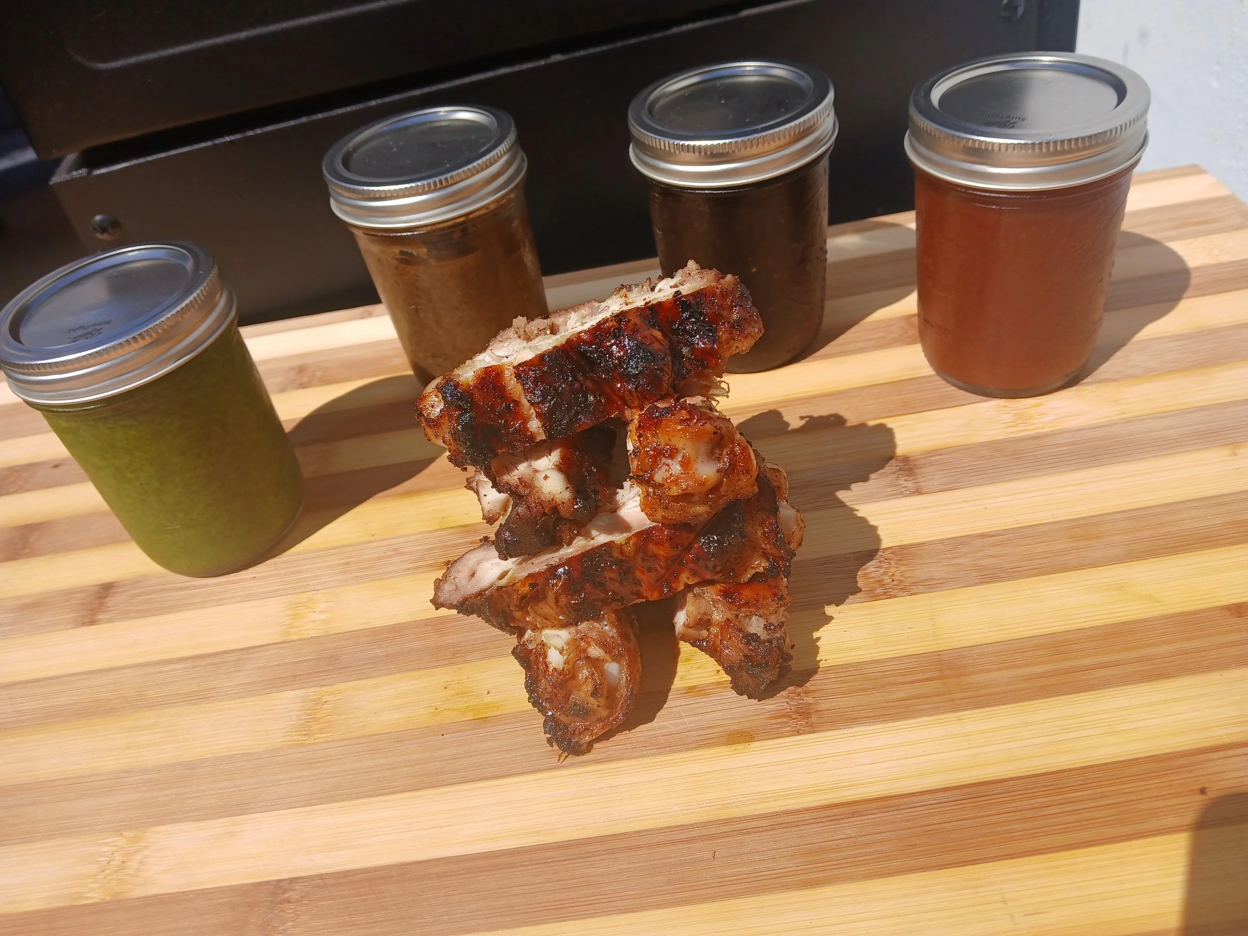 Barbecue chicken wings on a wooden serving board, with jars of different sauces behind them.