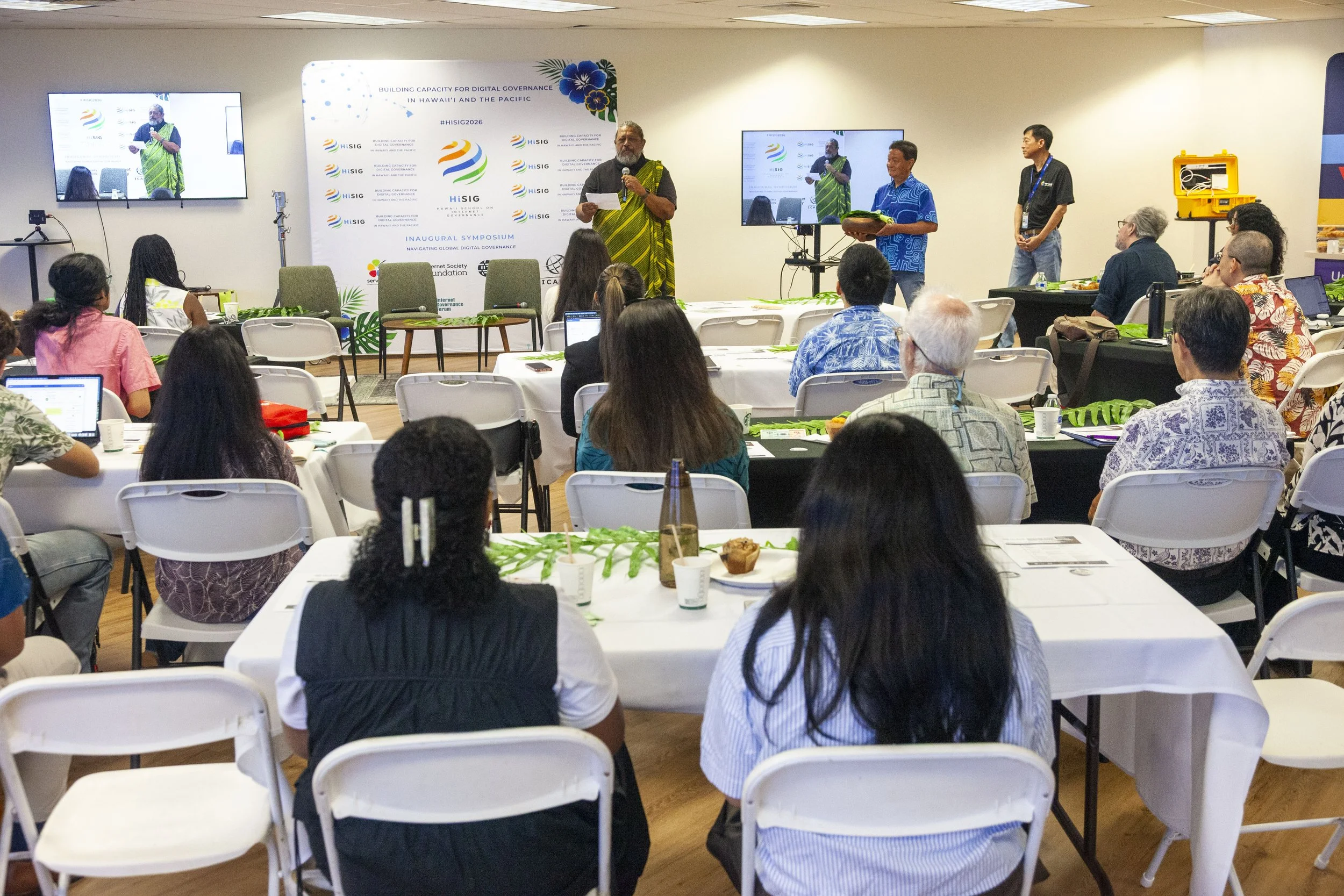 'HiSIG' conference. Honolulu, HI. The theme, 'Building Capacity for Digital Governance in Hawaii and the Pacific.' Attendees are seated, listening intently, with some taking notes or looking at their devices.