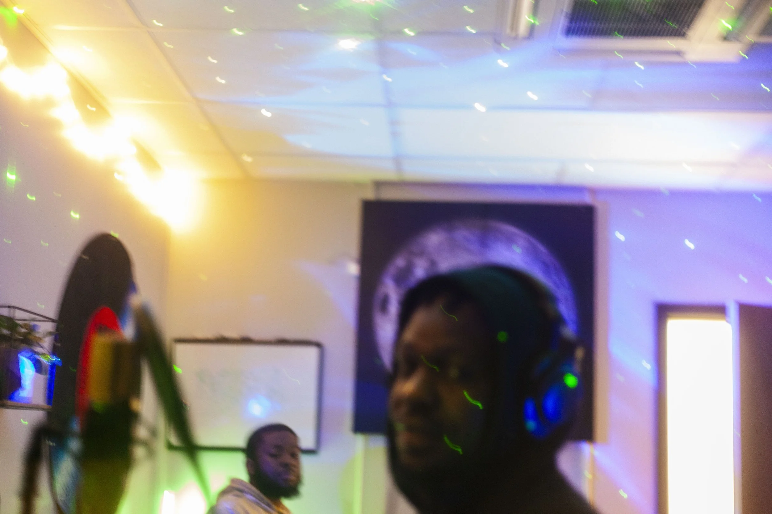 This$hitTuff. Charlotte, NC. .A dimly lit indoor setting with colorful lights and laser effects. There are a few people visible, including one person in the foreground wearing a bright shirt.