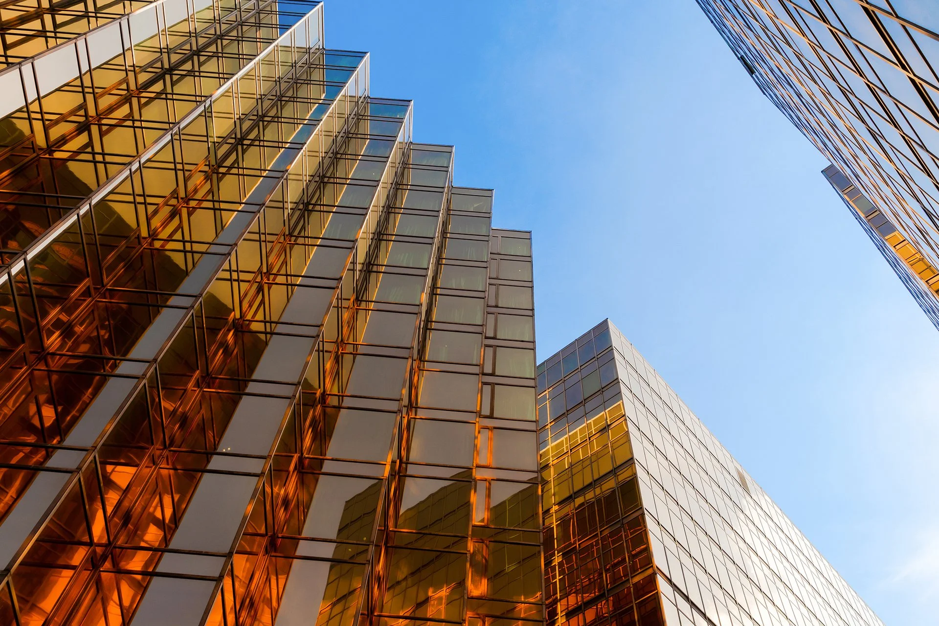 A low-angle view of modern glass office buildings with reflective windows and a clear blue sky background.