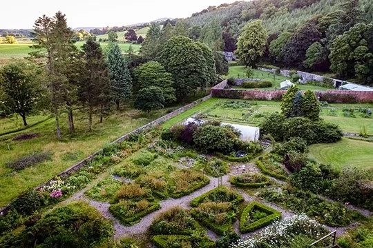 Aerial view of a large garden with divided sections, pathways, surrounded by trees and green fields.