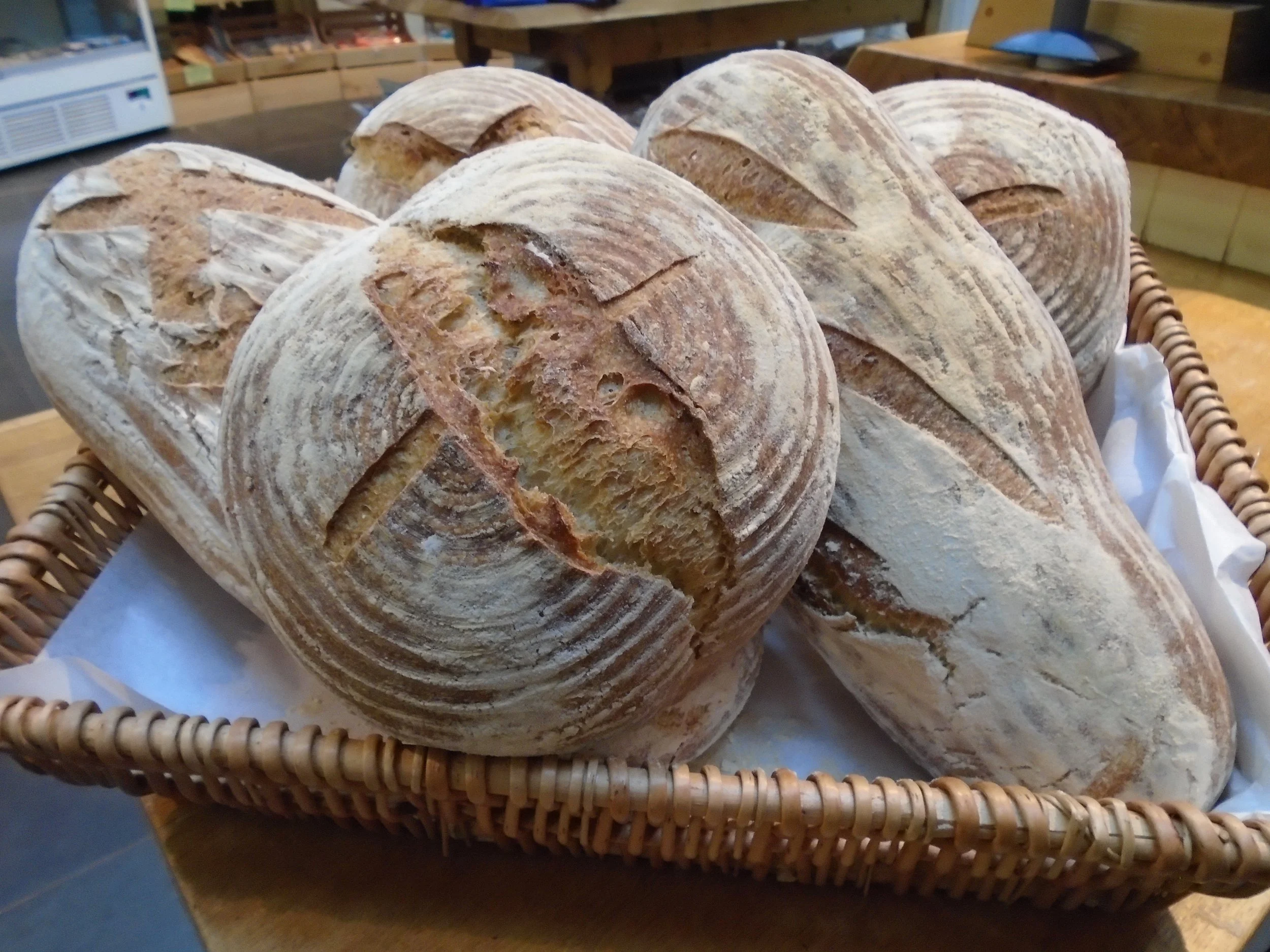 A basket of freshly baked rustic bread loaves with a dusting of flour, arranged in a display at a bakery.