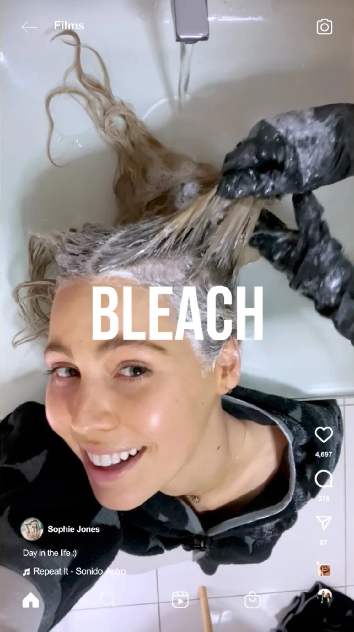 Person with blonde hair lying in a sink, receiving a bleach hair treatment, smiling at the camera.