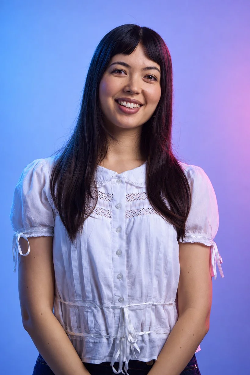 A young woman with long dark hair, smiling, wearing a white blouse, against a gradient background of blue and purple.