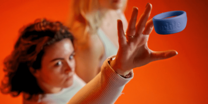 A woman with curly hair reaching out towards a blue silicone bracelet that is in mid-air against an orange background.