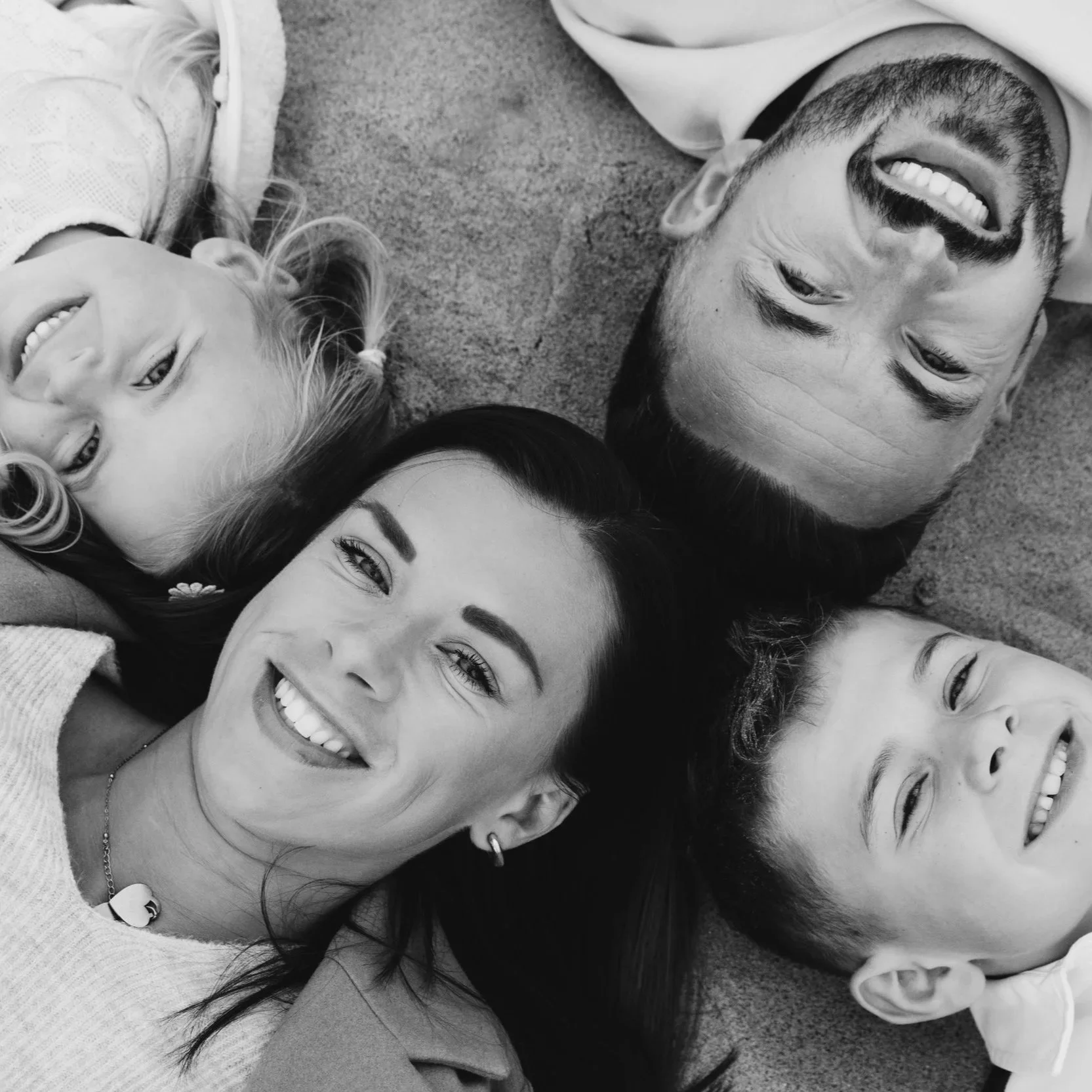 Black and white photo of a diverse group of five people lying on the floor, smiling and looking up at the camera.