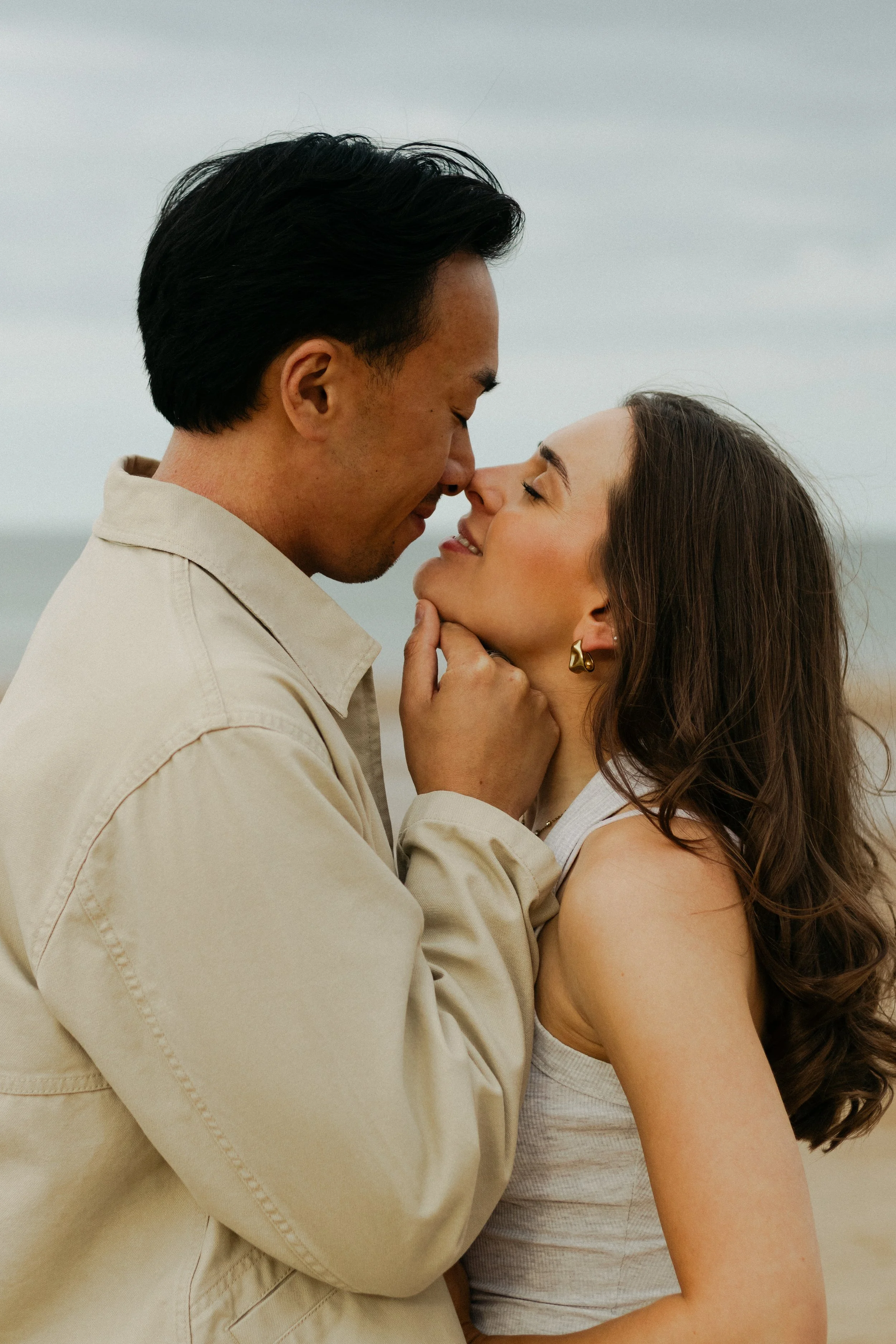 A couple sharing an intimate moment close to each other outdoors on a cloudy day.