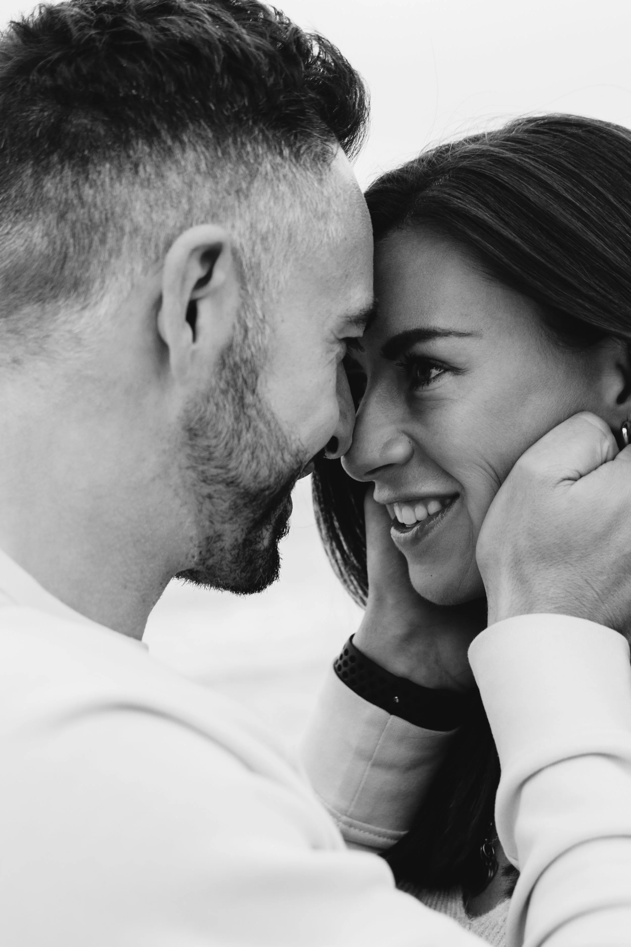 A black and white photo of a couple touching foreheads and smiling, with the man holding the woman's face gently.